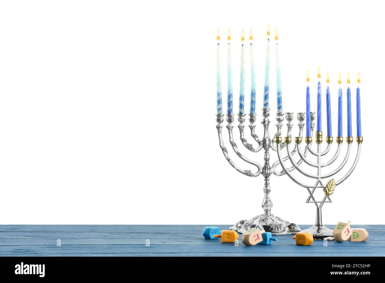 Hanukkah-Feier. Menorahs und Dreidels auf blauem Holztisch vor weißem Hintergrund Stockfoto