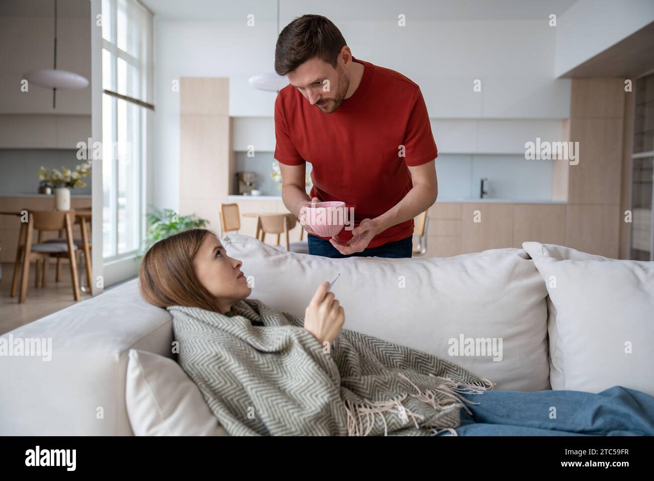 Liebevoller Ehemann, der eine Tasse heißen Tee hält, der für kranke Frau mit Grippe, Virus, covid, Fieber gemacht wurde Stockfoto