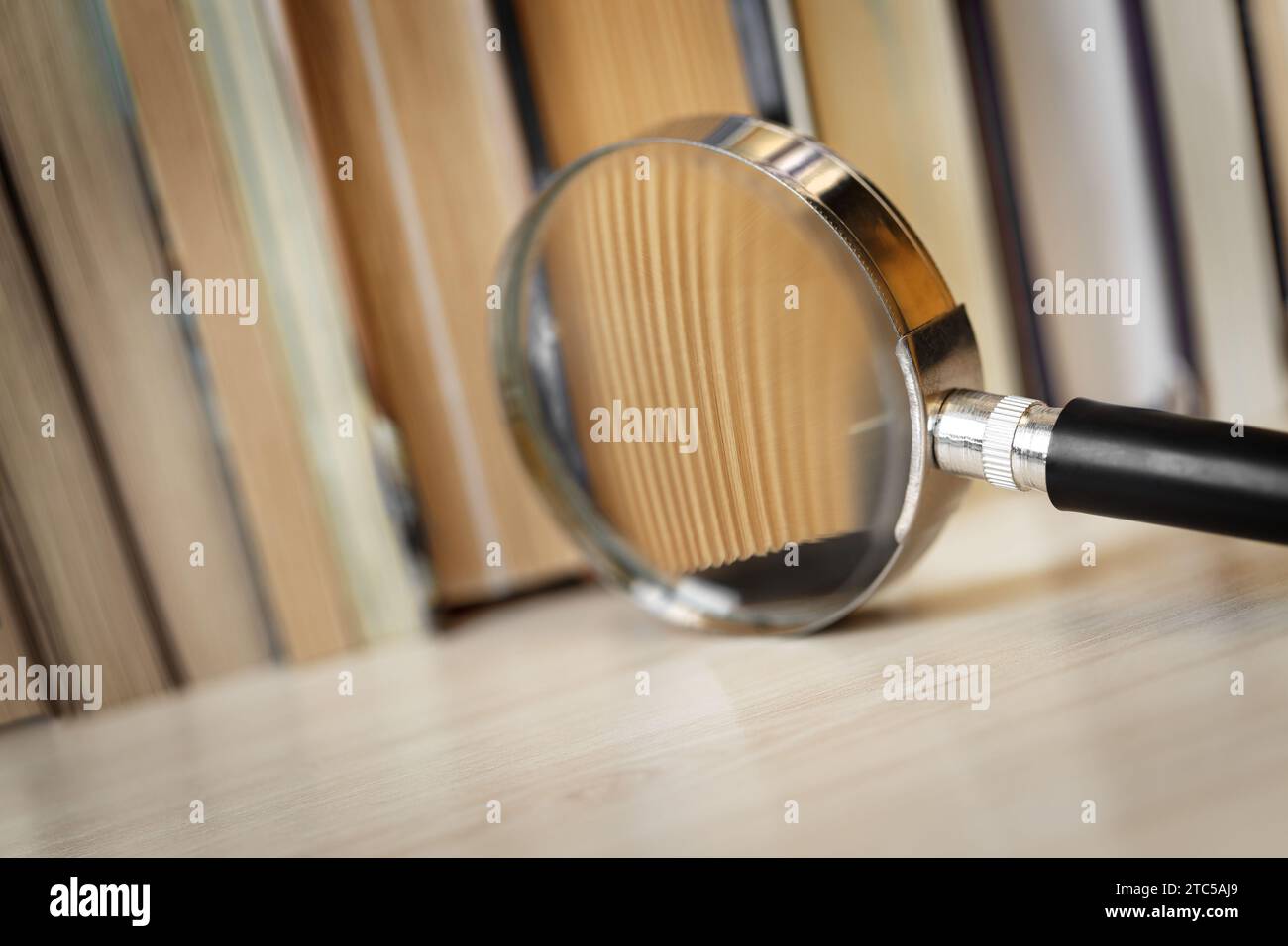 Bücher auf dem Tisch mit einem Fragment, das durch eine Lupe vergrößert wurde. Makrofotografie. Konzept der Forschung, Untersuchung und Suche nach Informationen Stockfoto