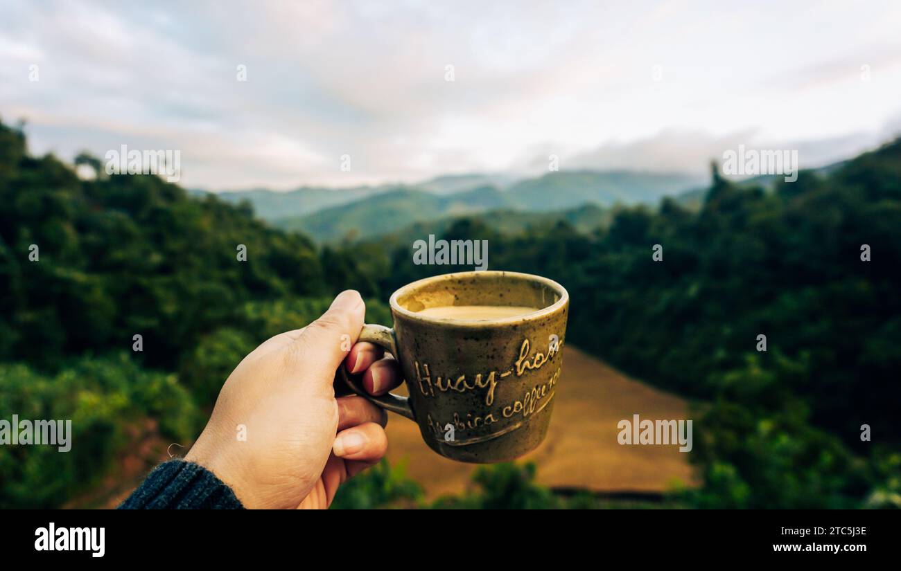 Hand hält eine Tasse Kaffee mit Aussicht. Heißer Espresso-Kaffee auf der Terrasse mit Blick auf die Reisfelder auf der Huay Hom Kaffeeplantage in Mae Hong Son Stockfoto