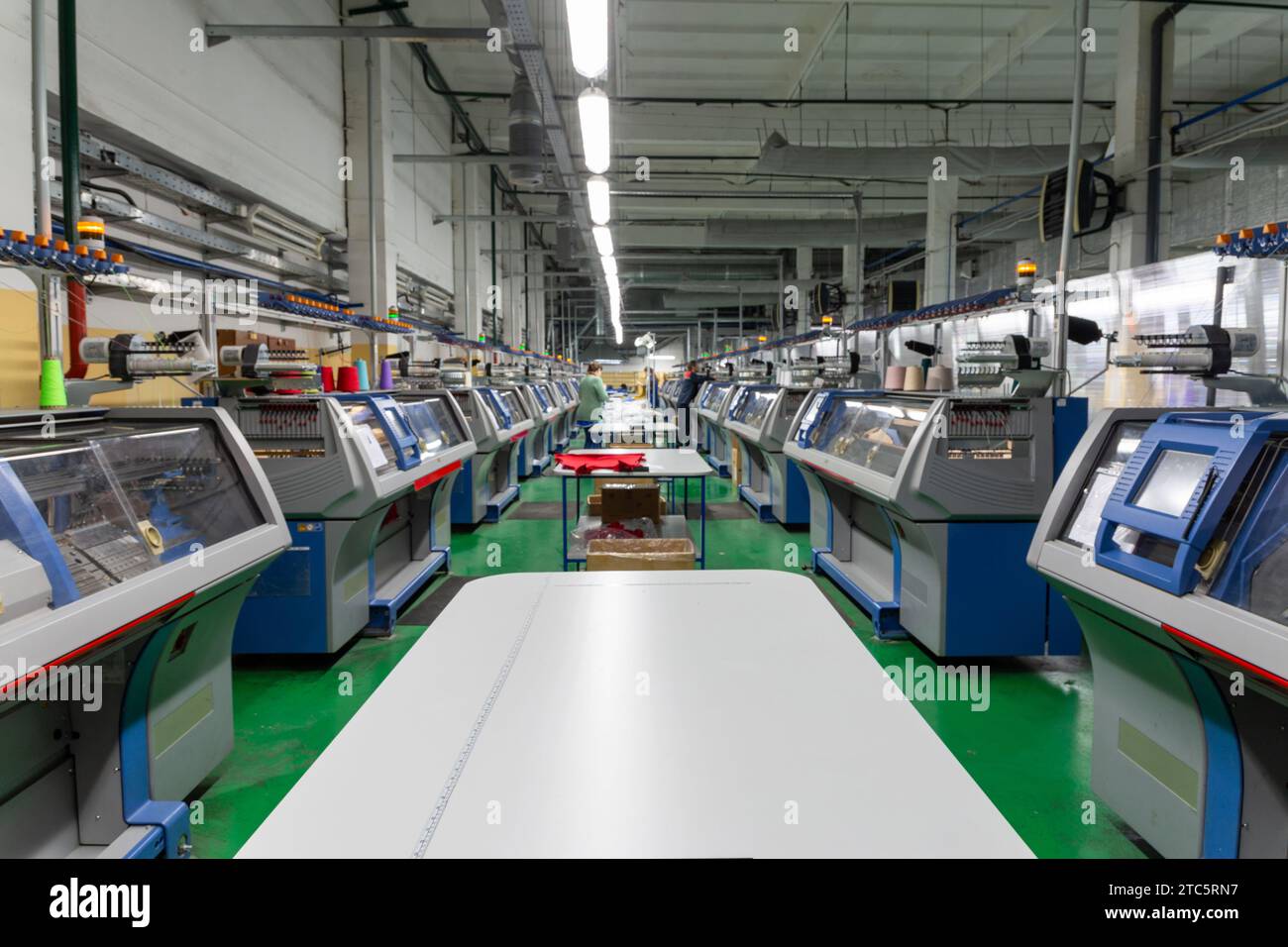 Eine Reihe industrieller Textil-Flachstrickmaschinen in einer Strickfabrik. Eine industrielle Linie moderner Strickautomaten, die in zwei Reihen angeordnet sind Stockfoto