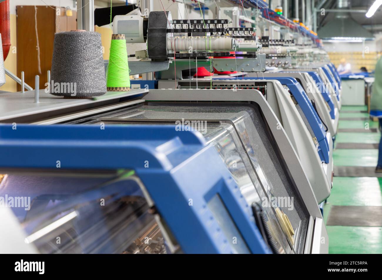 Eine Reihe industrieller Textil-Flachstrickmaschinen in einer Strickfabrik. Eine industrielle Linie moderner automatischer Strickmaschinen, die in einer Reihe angeordnet sind. Stockfoto