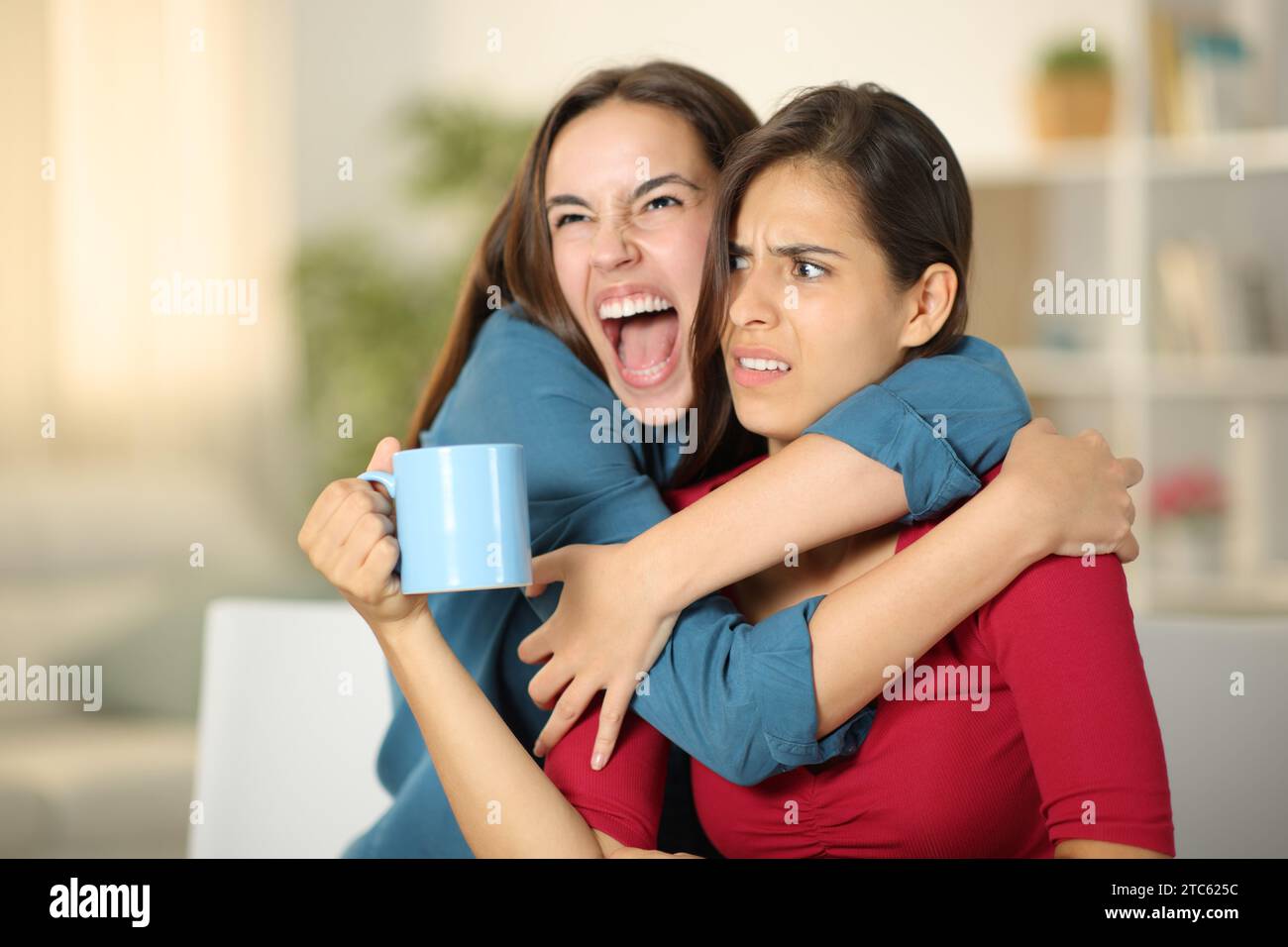 Aufgeregte Frau, die zu Hause einen verärgerten Freund umarmt Stockfoto