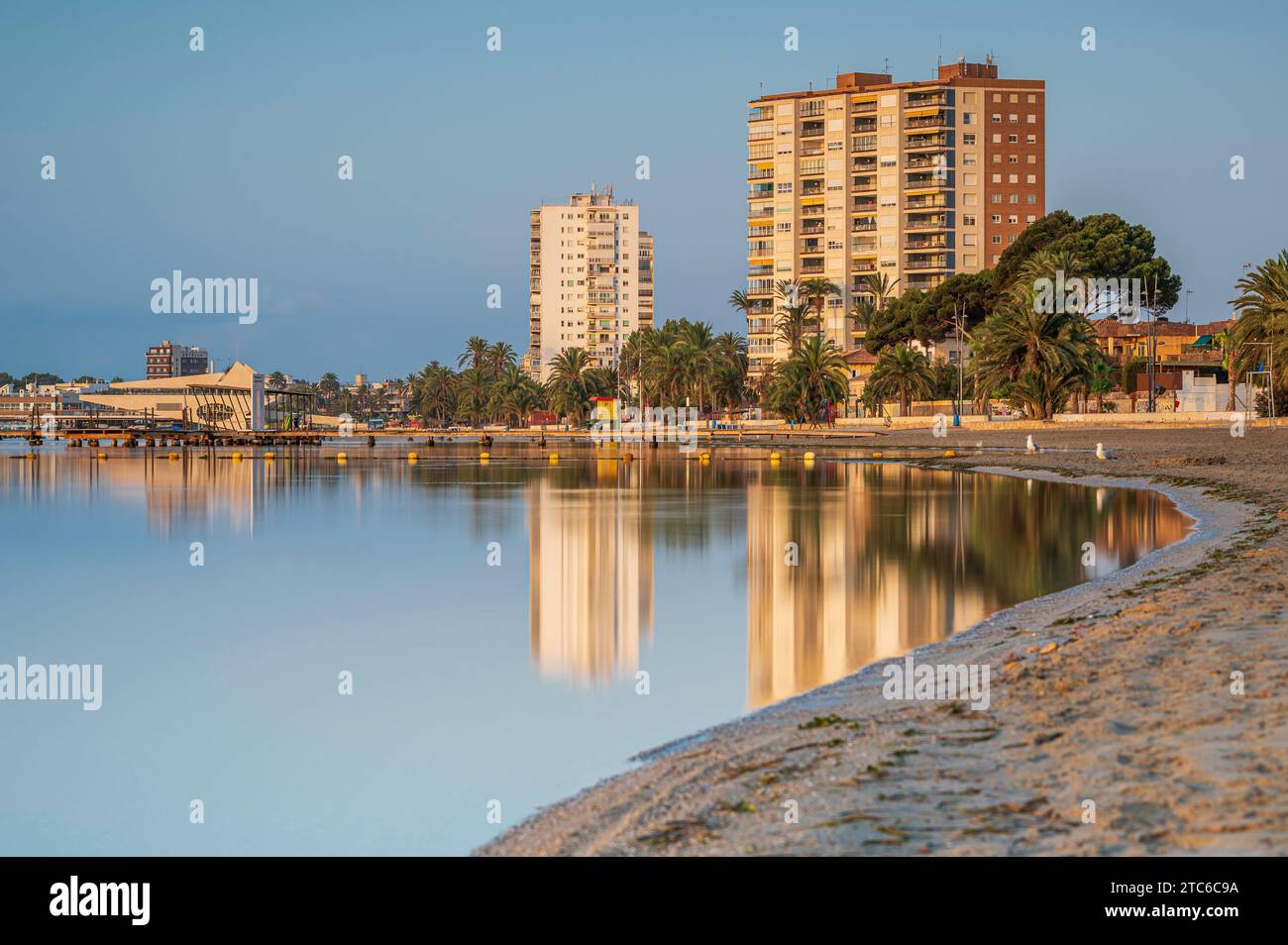 Hochhaus, entlang eines spanischen Strandes, das sich bei Sonnenaufgang im ruhigen Meer spiegelt Stockfoto