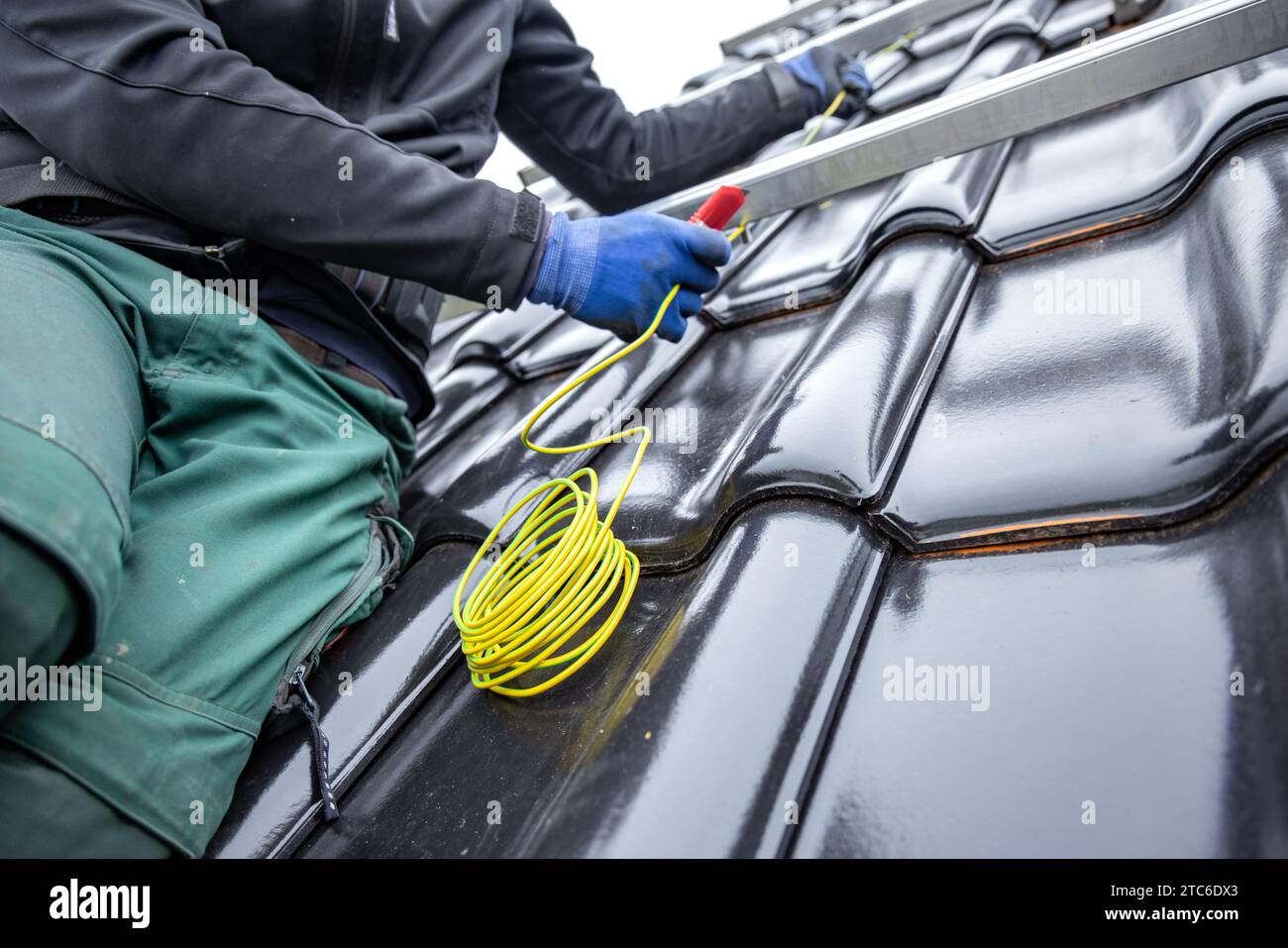 Techniker, der Kabel für die Installation von Sonnenkollektoren auf einem gekachelten Dach verlegt Stockfoto