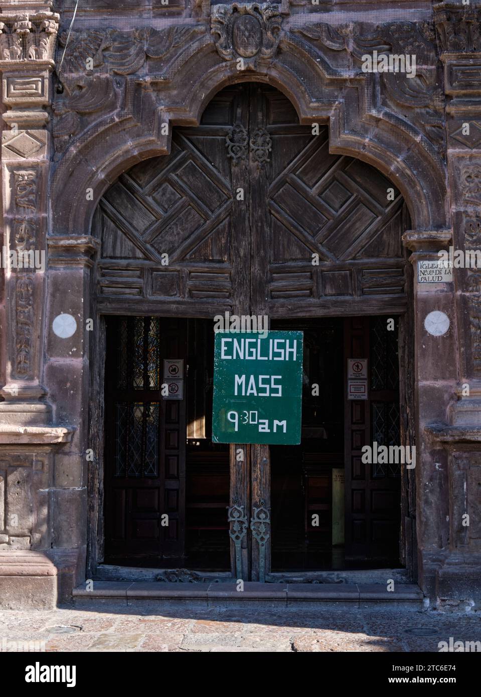 Kirchentür in San Miguel de Allende, Mexiko, kündigt am Sonntag eine englische Messe an Stockfoto