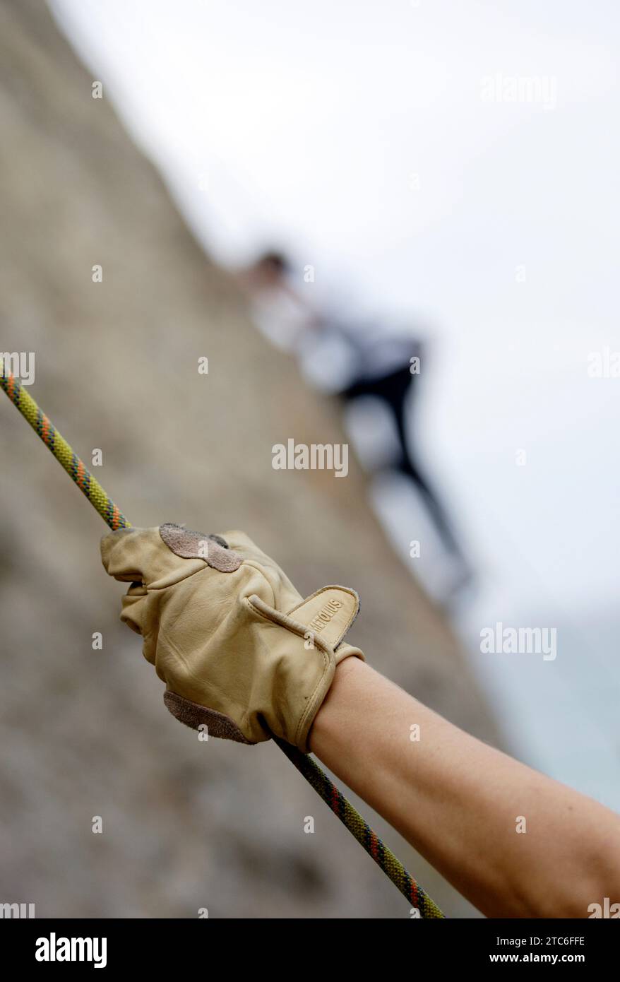 Eine Hand greift ein Seil, während eine Person im Hintergrund eine Felswand in Malibu, Kalifornien, bestiegen. (Ausgewählter Fokus) Stockfoto