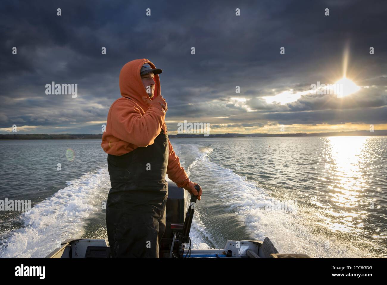 Kommerzielle Fischer mit Wathose in einem Fischerboot mit stürmischem Himmel Stockfoto