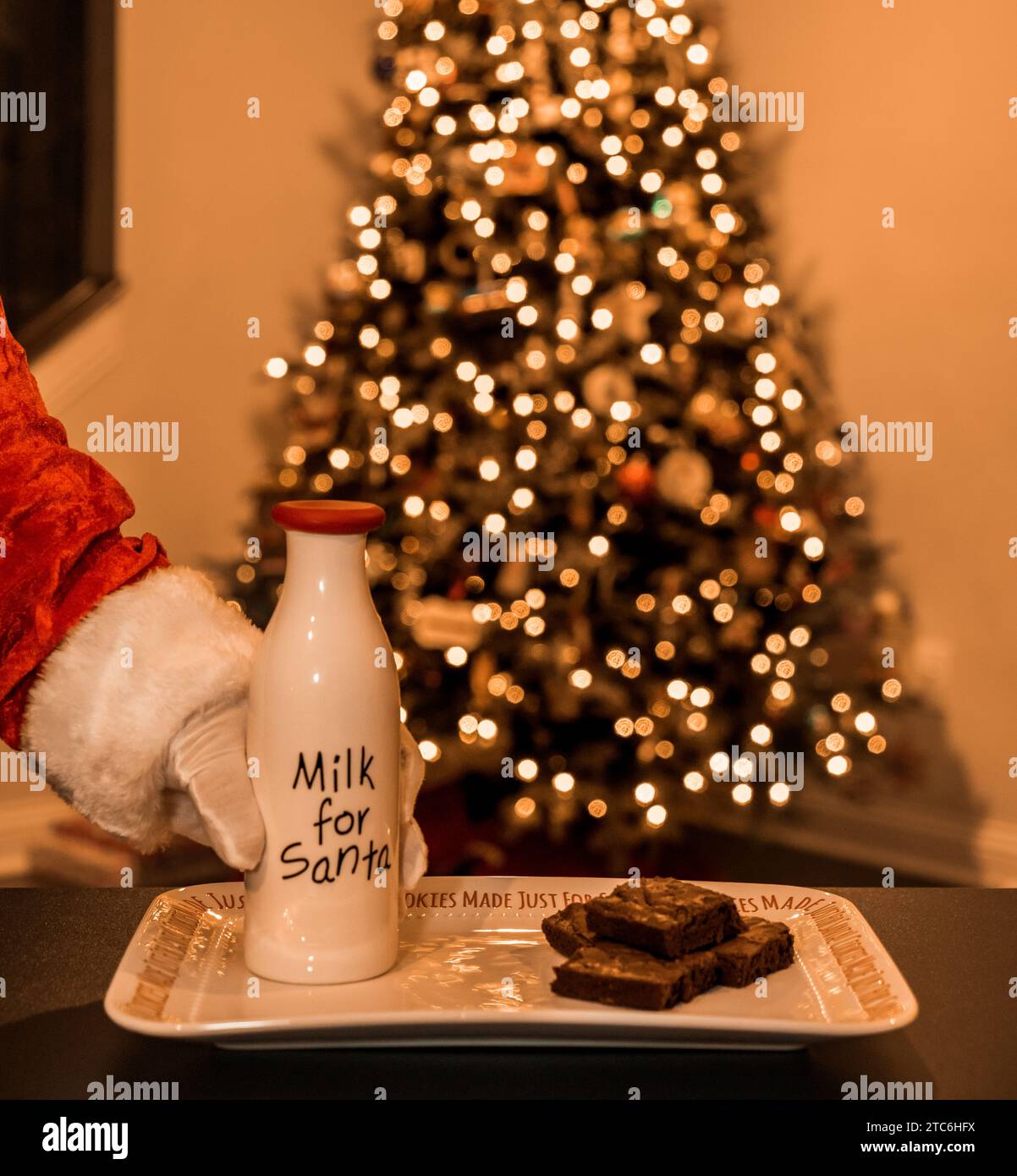 Die Weihnachtsmann-Hand greift nach der Milchflasche mit Brownies auf dem Teller Stockfoto