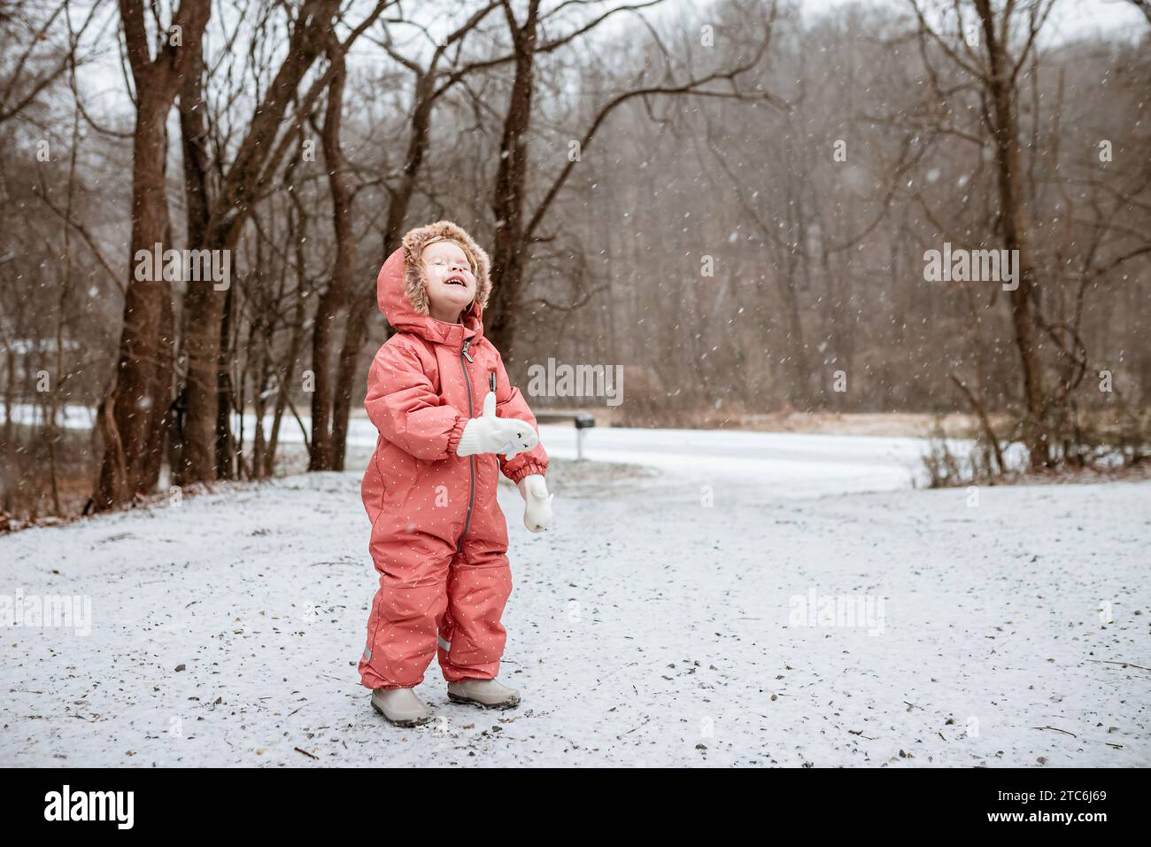 Lächelndes Kind, das während des Winters in den Schnee blickt Stockfoto