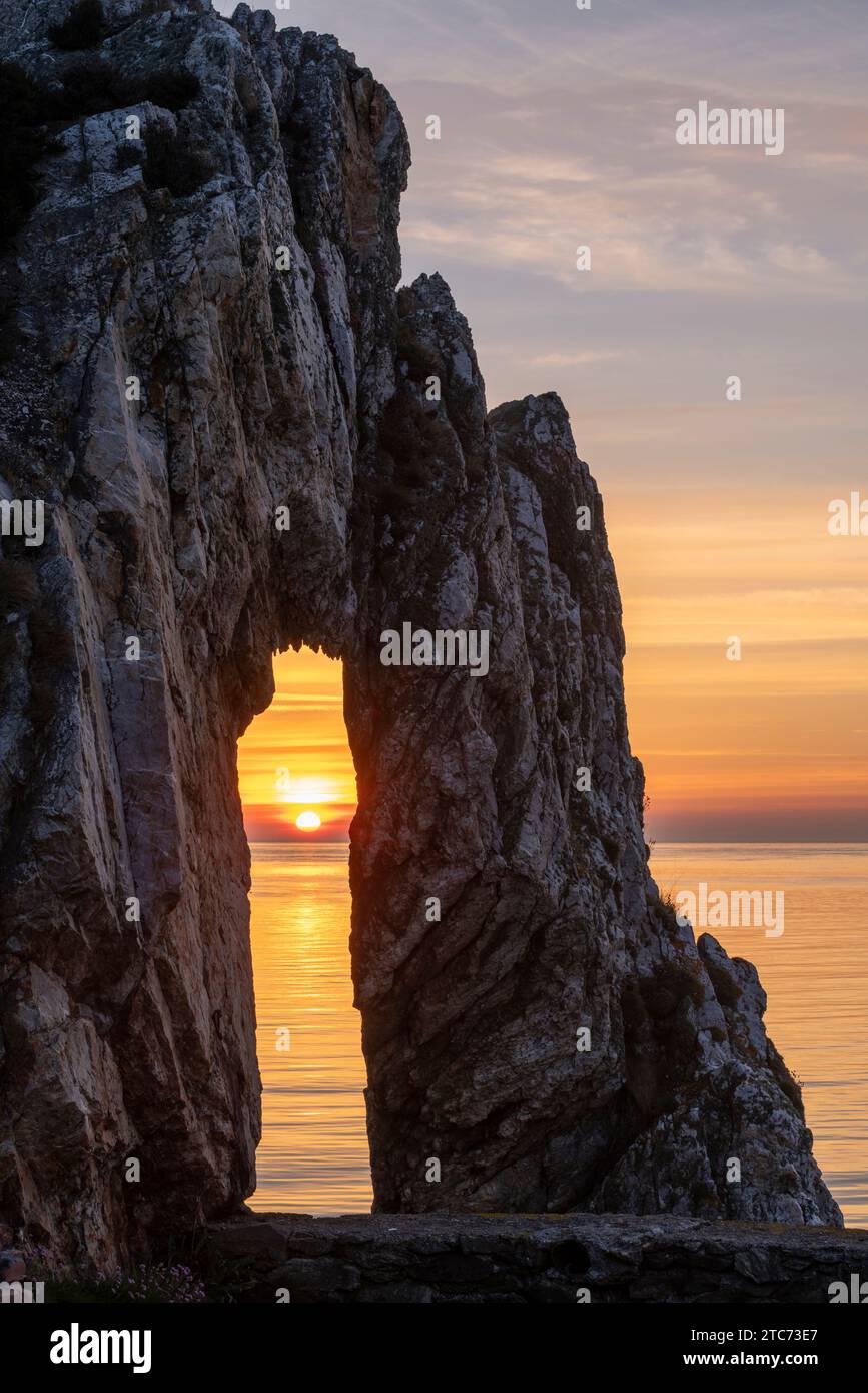 Sonnenaufgang durch einen Felsbogen am viktorianischen Ziegelwerk in Porth Wen, Anglesey, Wales, Großbritannien. Frühjahr (Mai) 2019. Stockfoto