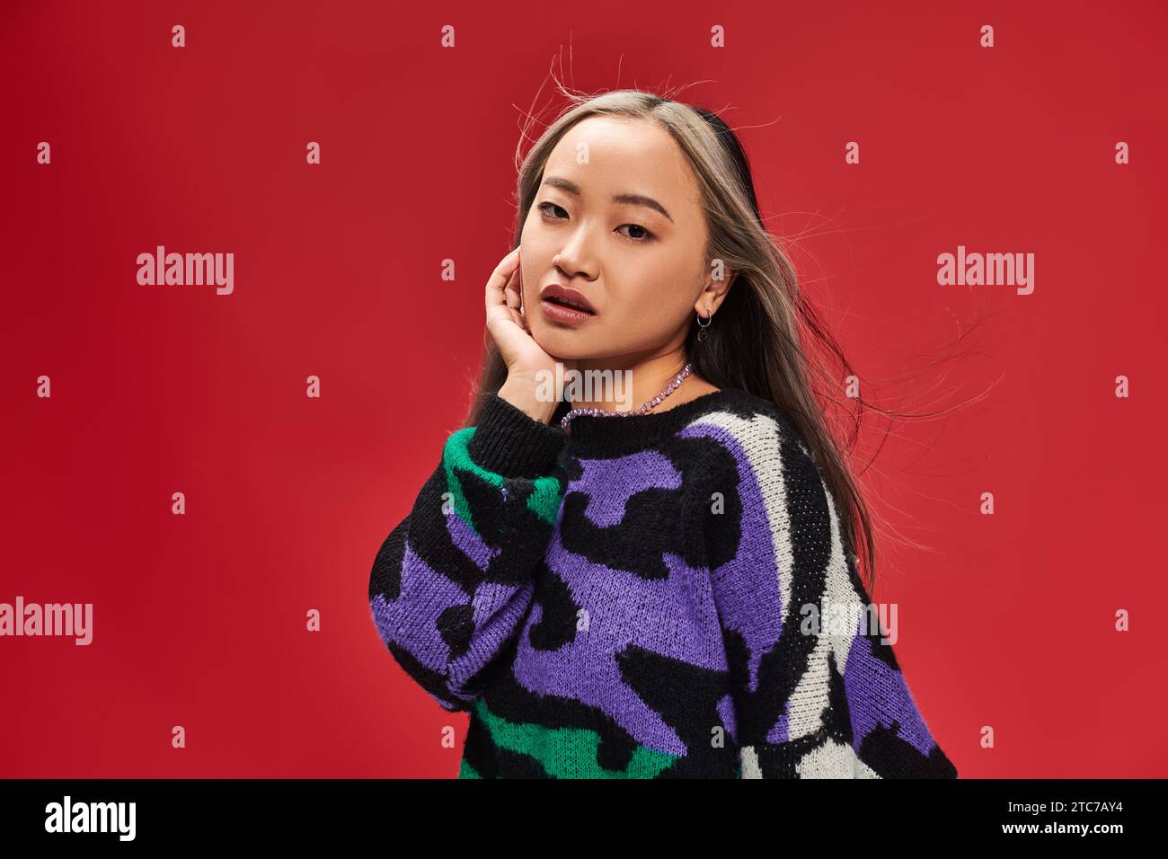 Schöne junge asiatische Frau mit gefärbten Haaren im Pullover mit Tierdruck posiert mit Hand nahe Gesicht Stockfoto