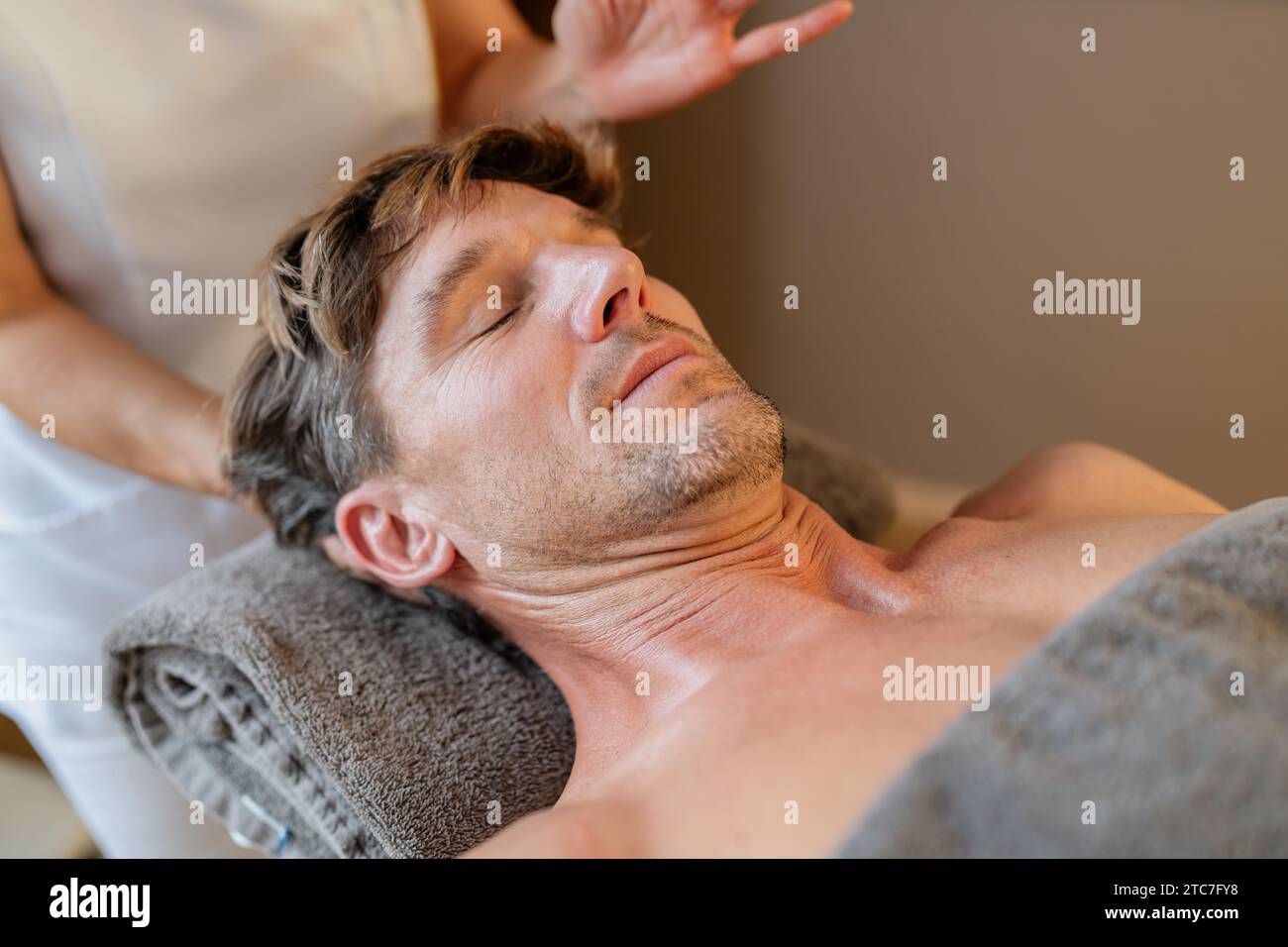 Entspannter Mann, der eine Nackenmassage von einem Therapeuten mit verschwommenen Händen erhält Stockfoto