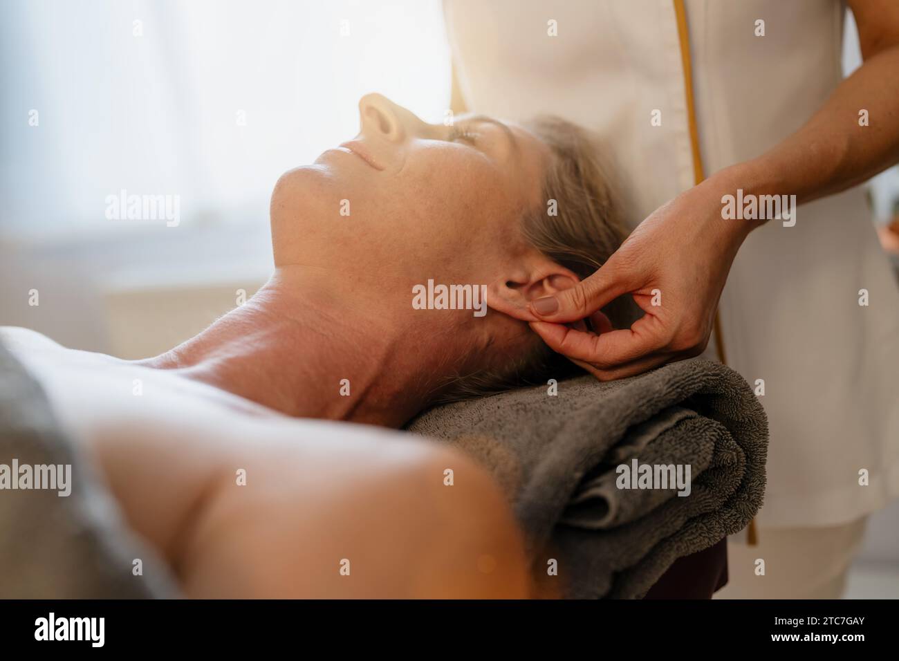 Seitenansicht eines Massage-Therapeuten, der eine Ohrmassage für eine entspannte Kundin in einem Schönheitssalon durchführt Stockfoto