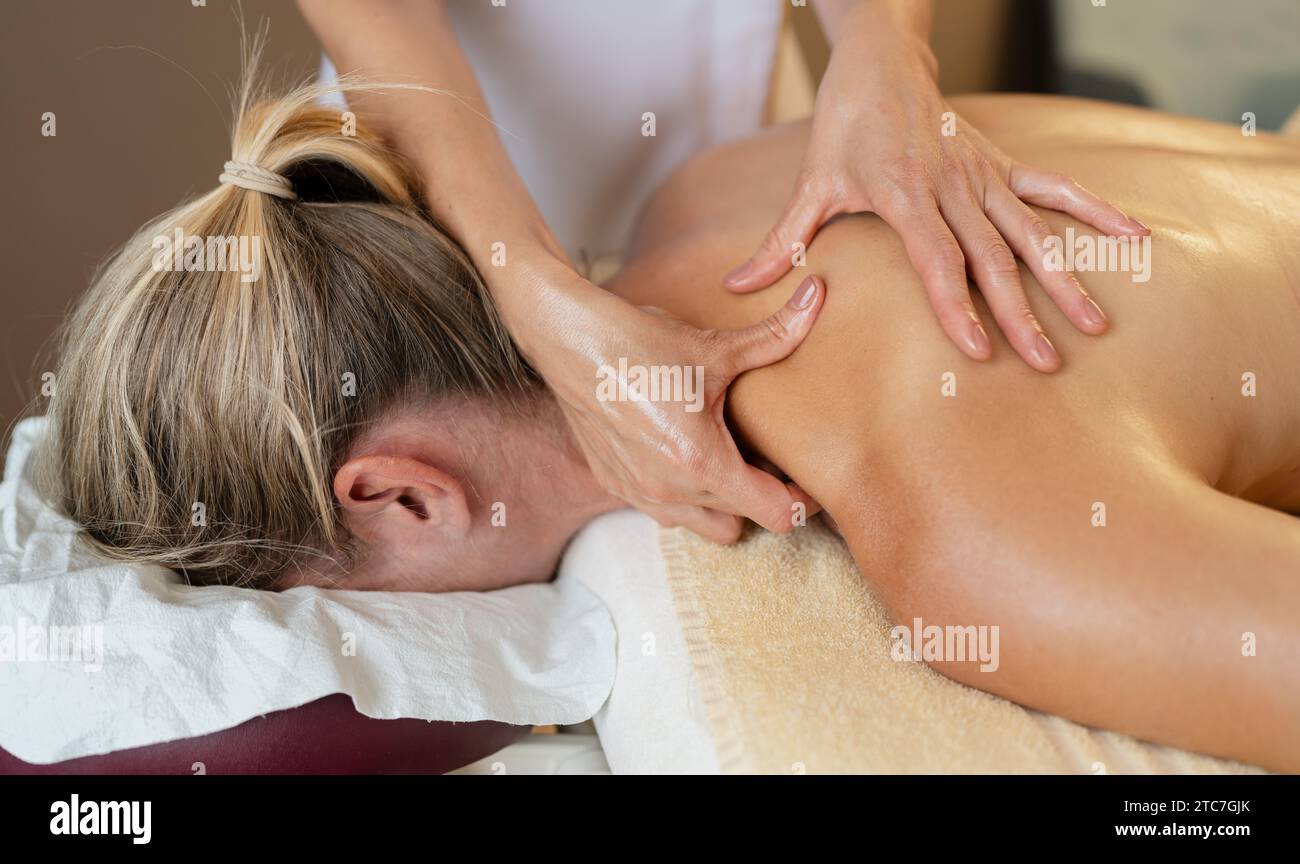 Massagetherapeutin, die eine Schulter- und Rückenmassage bei einer anfälligen Frau anwendet. Schönheitssalon Wellness Hotel Konzept Bild Stockfoto