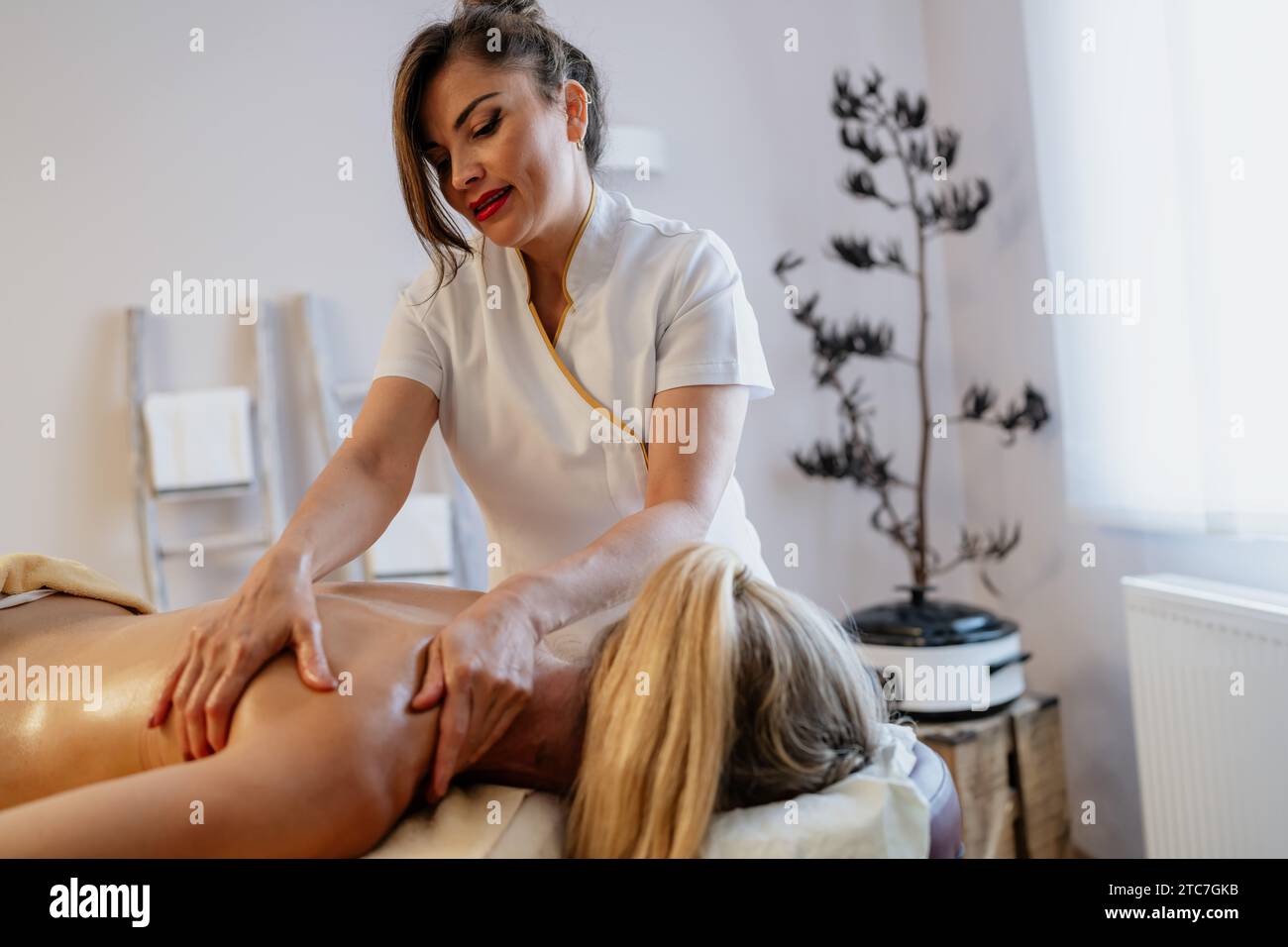 Konzentrierter Massagetherapeut, der eine Rückenmassage in einem gut beleuchteten Wellnesshotel durchführt Stockfoto