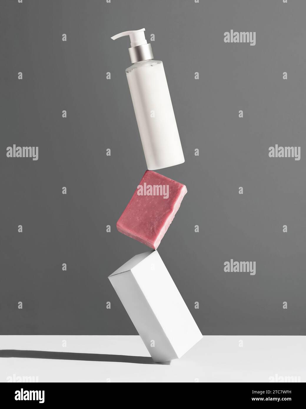 Creative Concept Körperpflege. Weiße Flasche, Stück Seife und Box für Kosmetikprodukte, die vor grauem Hintergrund aufeinander balanciert sind. Stockfoto