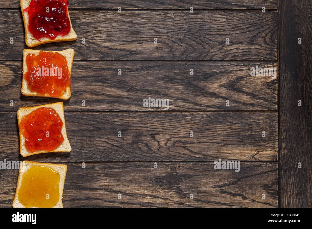 Vier geröstete Brote mit verschiedenen Marmeladen auf der linken Seite des Tisches, Draufsicht Stockfoto