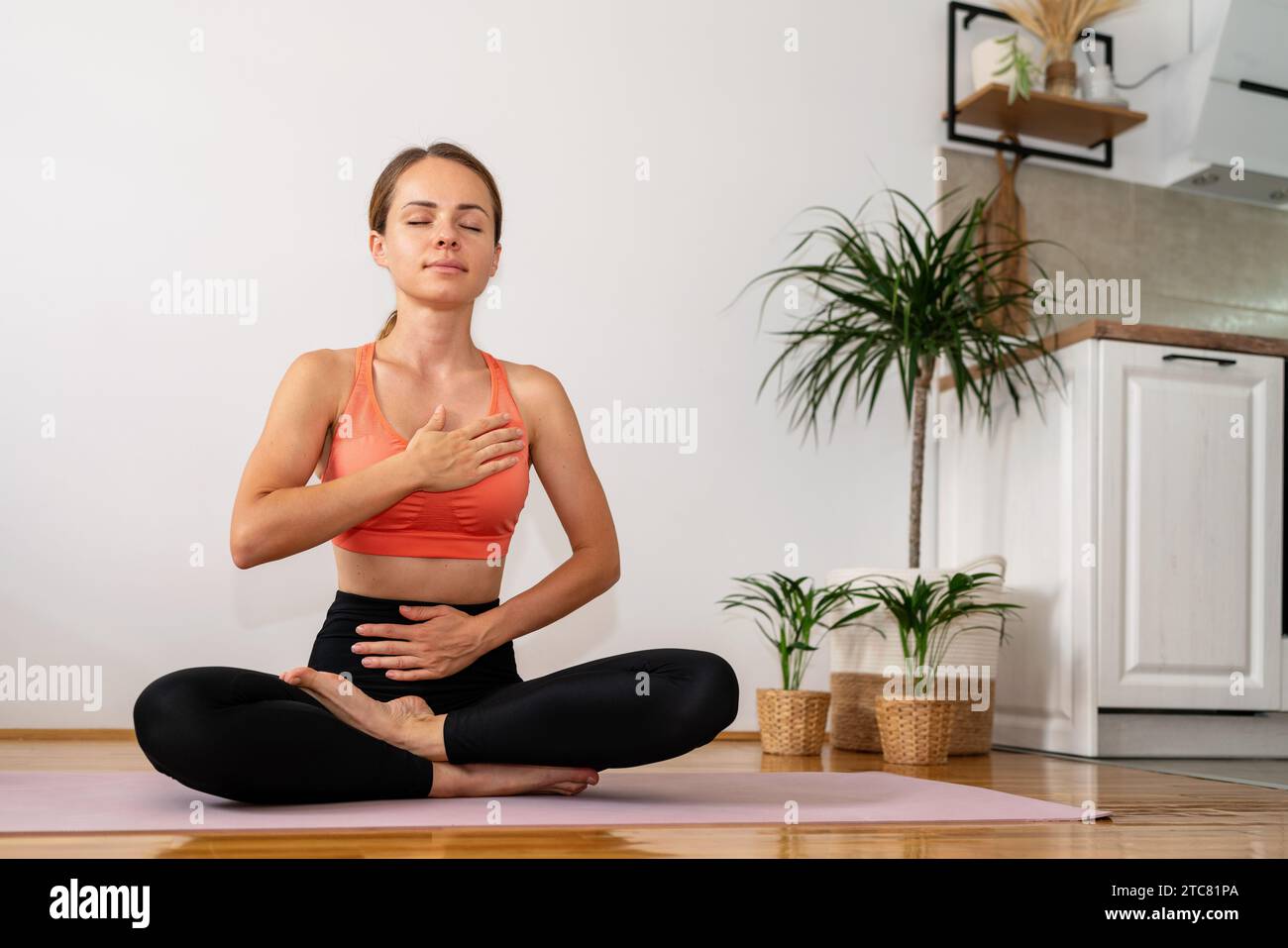 Ruhige Meditation zu Hause mit Yoga. Frau, die Atemübungen macht, während sie in Lotusposition auf Yogamatte sitzt. Stockfoto
