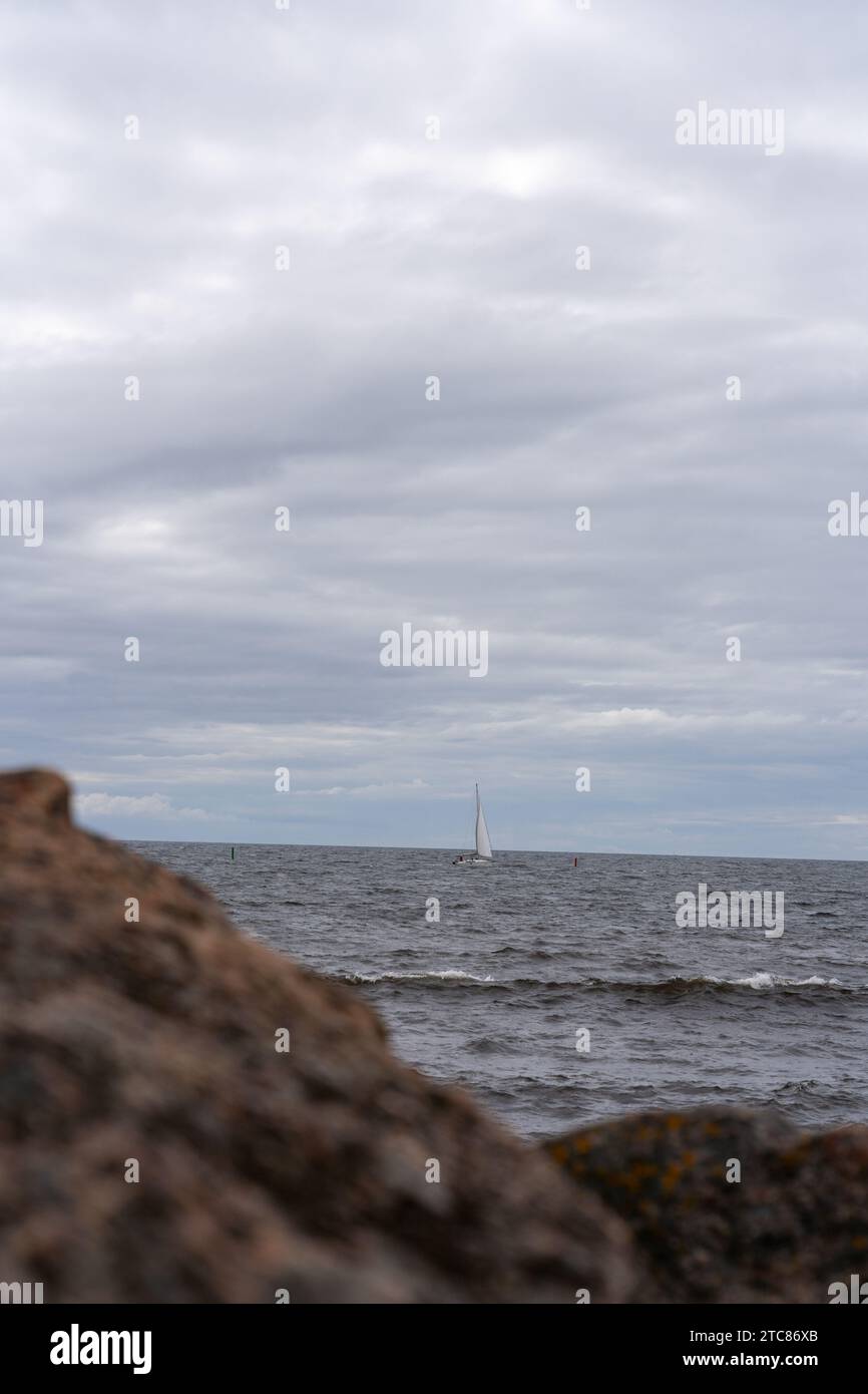 Ein weißes Segelboot ist in der Ferne auf einem ruhigen Gewässer zu sehen, mit einem klaren blauen Himmel über Varberg, Schweden Stockfoto