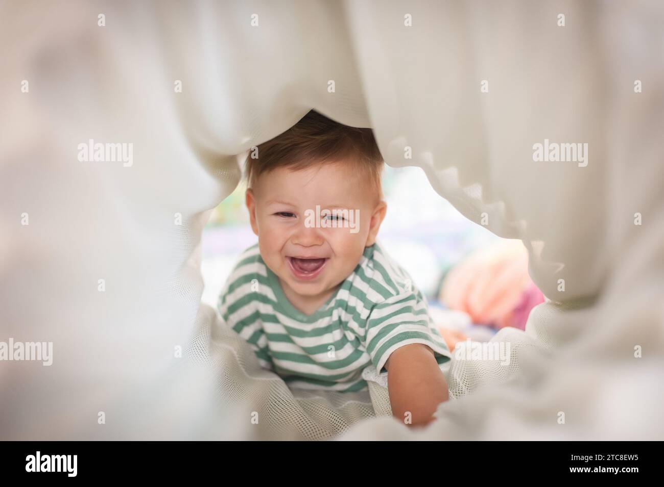 Süßes, glückliches, lachendes Baby, das durch den Spieltunnel kriecht. Kindliche Entwicklung. Glücksgefühl und Menschenkonzept Stockfoto