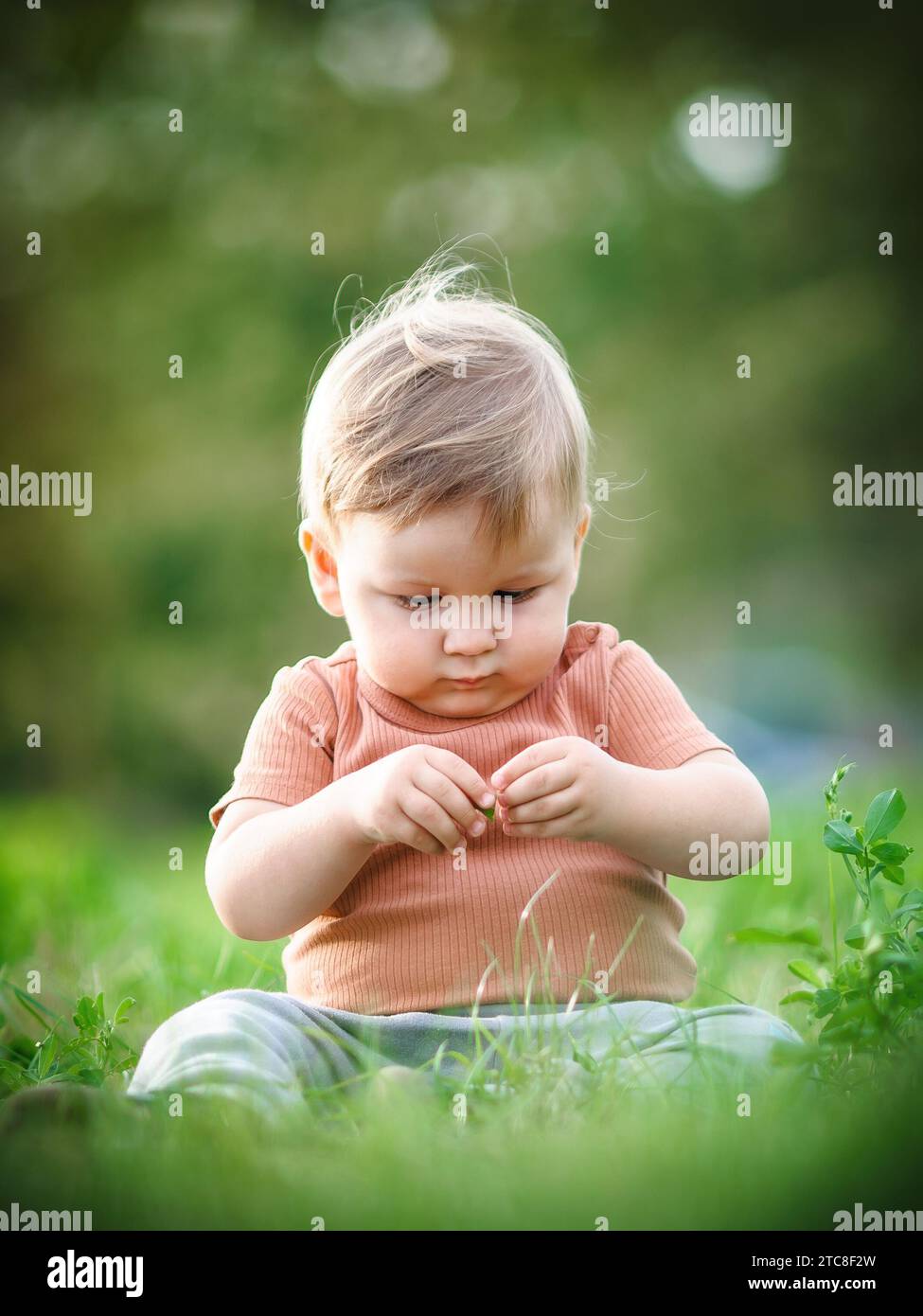 Niedliches Baby, das Spaß am Sonnenschein hat, auf Gras zu sitzen. Sommerzeit, glückliches Baby Stockfoto