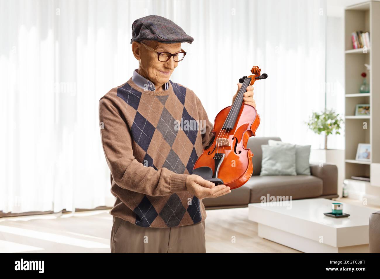 Ein älterer Mann, der zu Hause im Wohnzimmer eine Geige hält Stockfoto