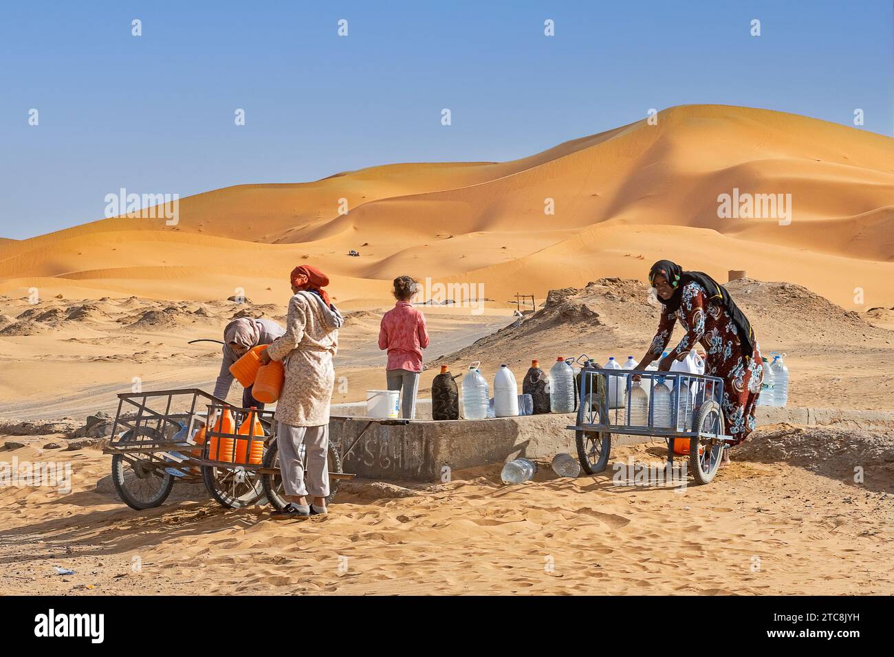Marokkanische Berberfrauen sammeln Trinkwasser aus Brunnen in Erg Chebbi in der Sahara bei Merzouga, Drâa-Tafilalet, Errachidia, Marokko Stockfoto