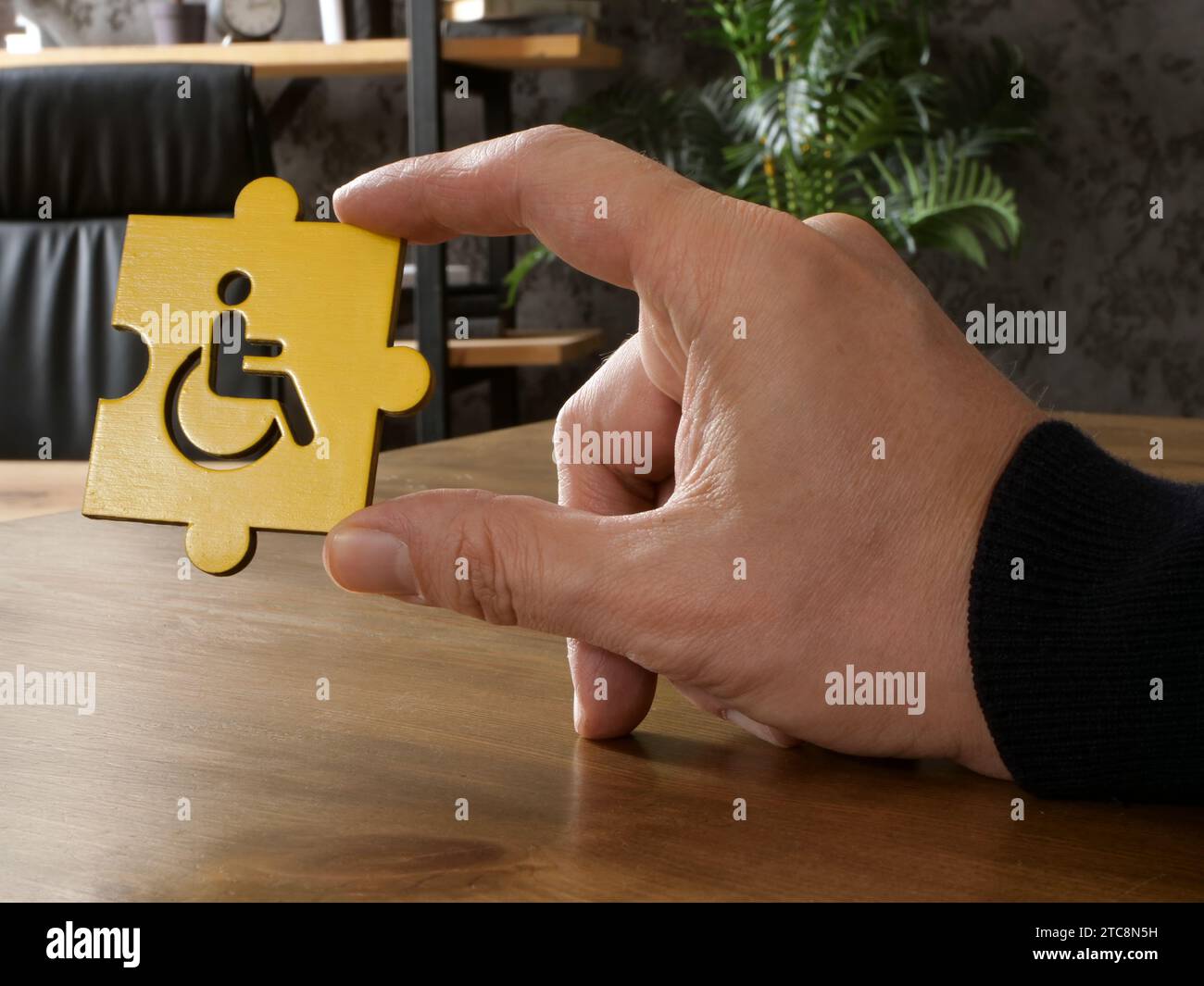 Eine Hand hält das Puzzleteil mit dem Symbol einer behinderten Person. Integratives Arbeitsplatzkonzept. Stockfoto
