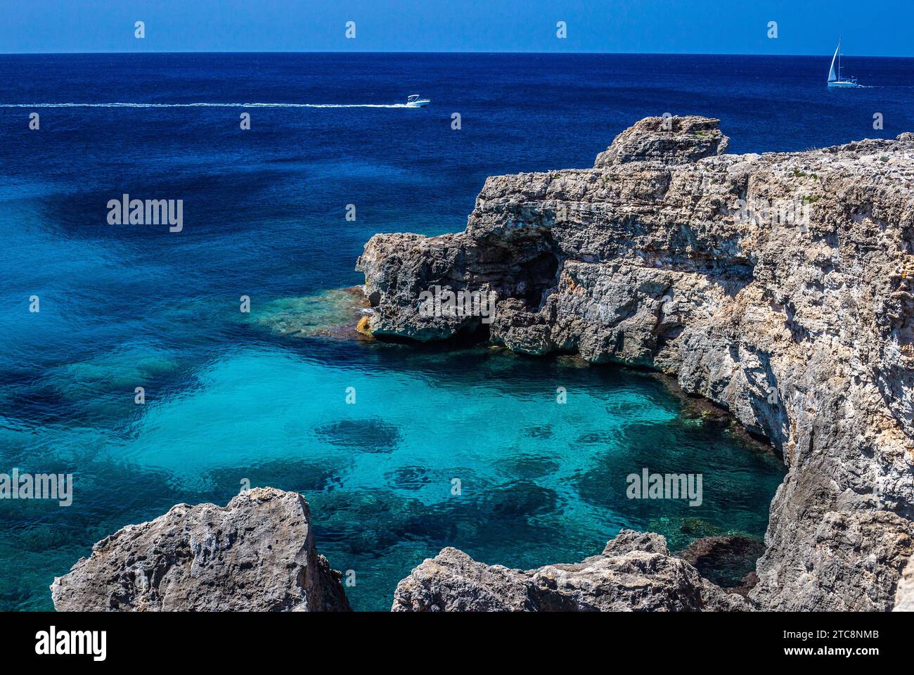 Wunderschönes Binibeca ein weißes, stilvolles Dorf an der Küste Menorcas, wo das blaue Meer die rauen Felsformationen berührt und Yachten friedlich vorbeisegeln Stockfoto