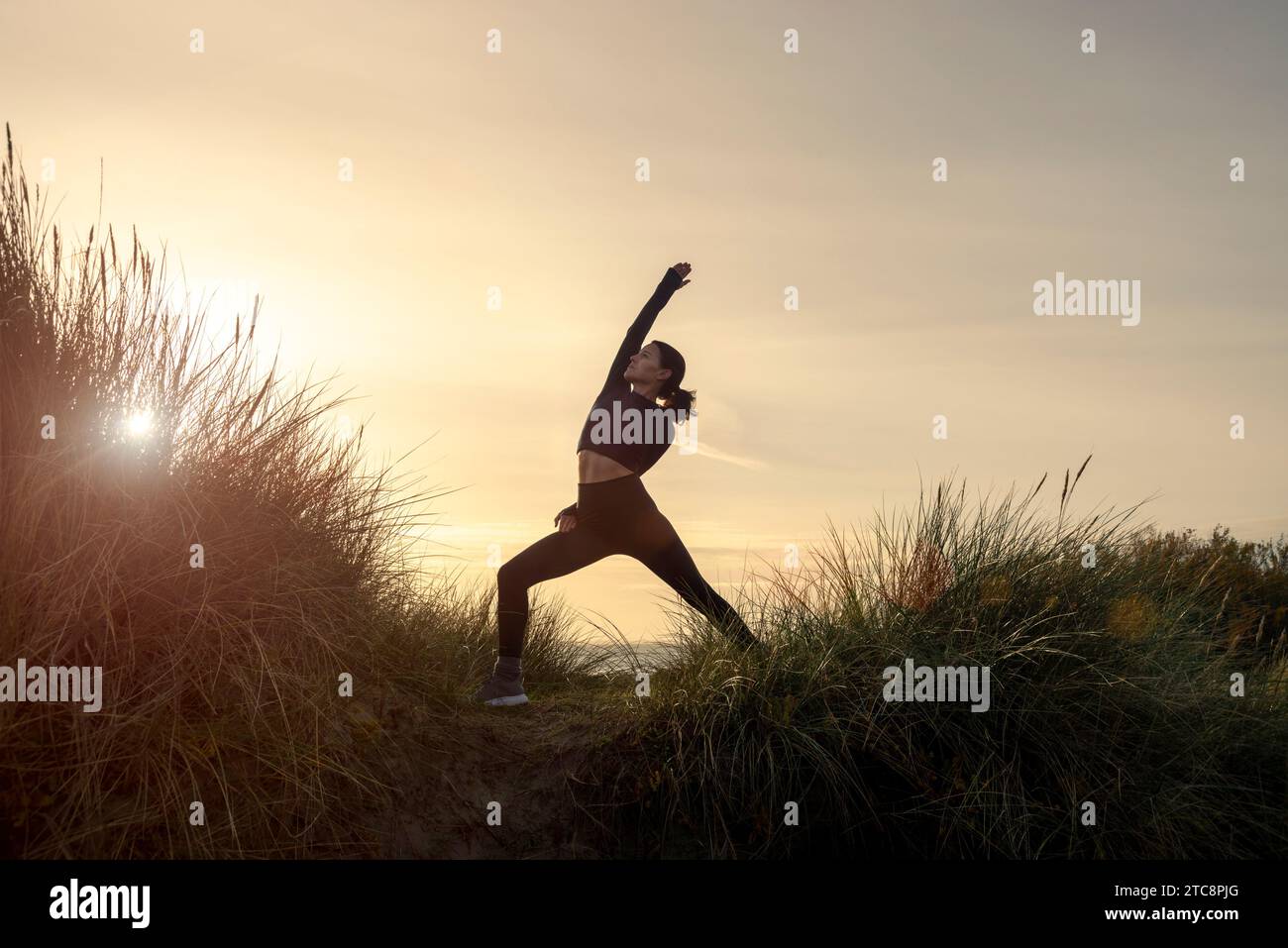 Frau, die draußen bei Sonnenaufgang Yoga macht, umgekehrte Kriegerposierung. Stockfoto