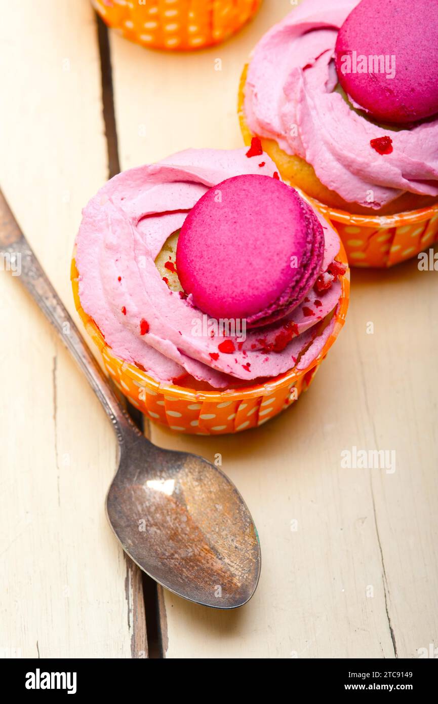 Frischer rosa Beerencreme-Cupcake mit Makronen auf dem rustikalen Holztisch Stockfoto