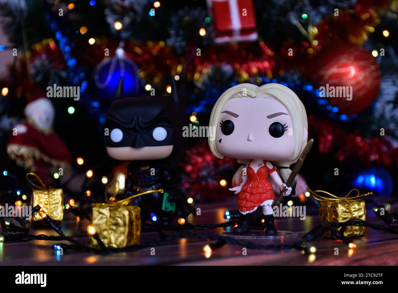 Funko Pop Actionfiguren der DC Comics Superhelden Batman und Harley Quinn. Weihnachtsbaum, Ornamente, Girlande, Geschenkboxen, bunte Lichter. Stockfoto