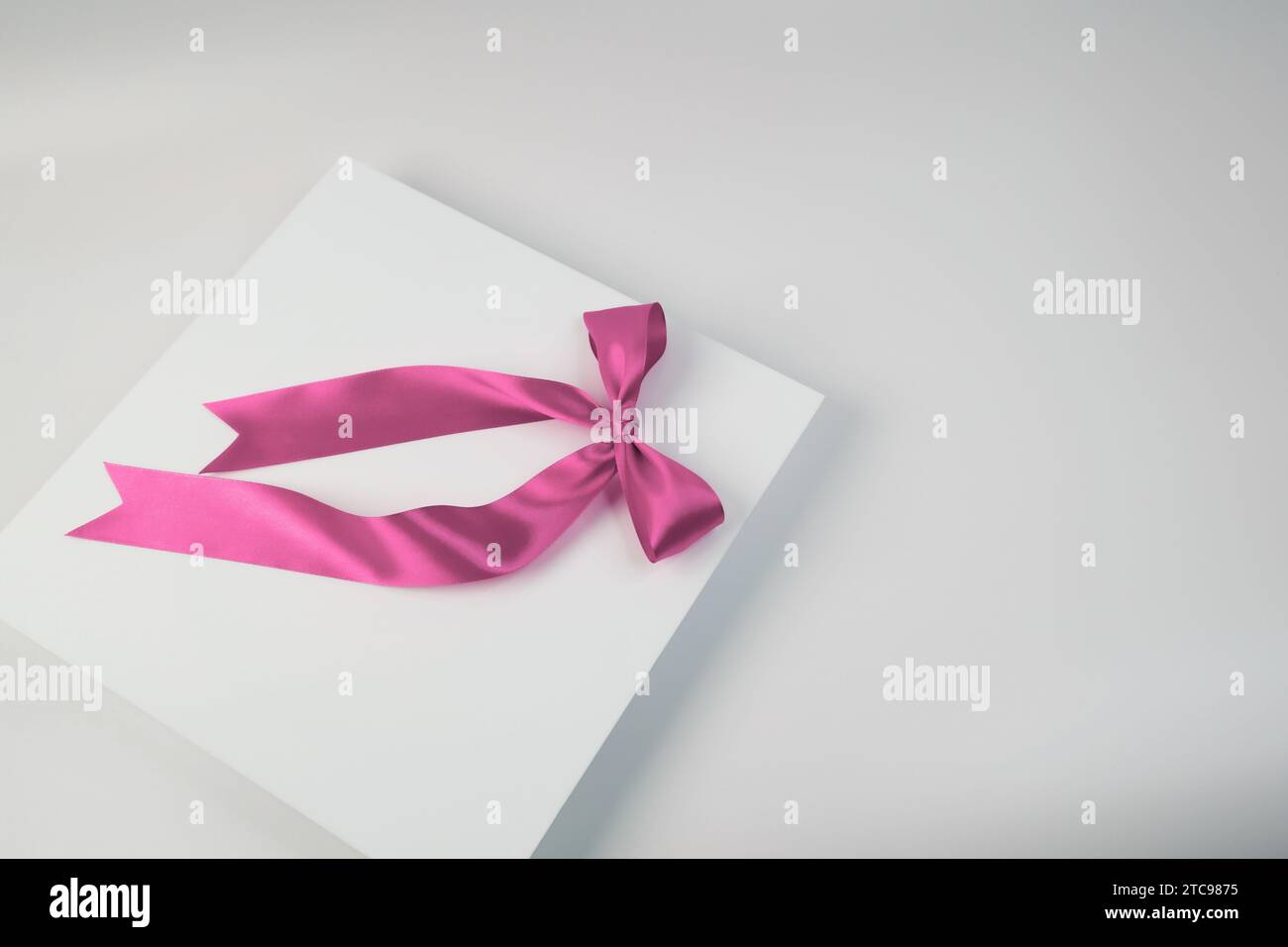 Eine weiße Geschenkbox, gebunden mit einem rosafarbenen Band, sitzt auf einem weißen Hintergrund Stockfoto