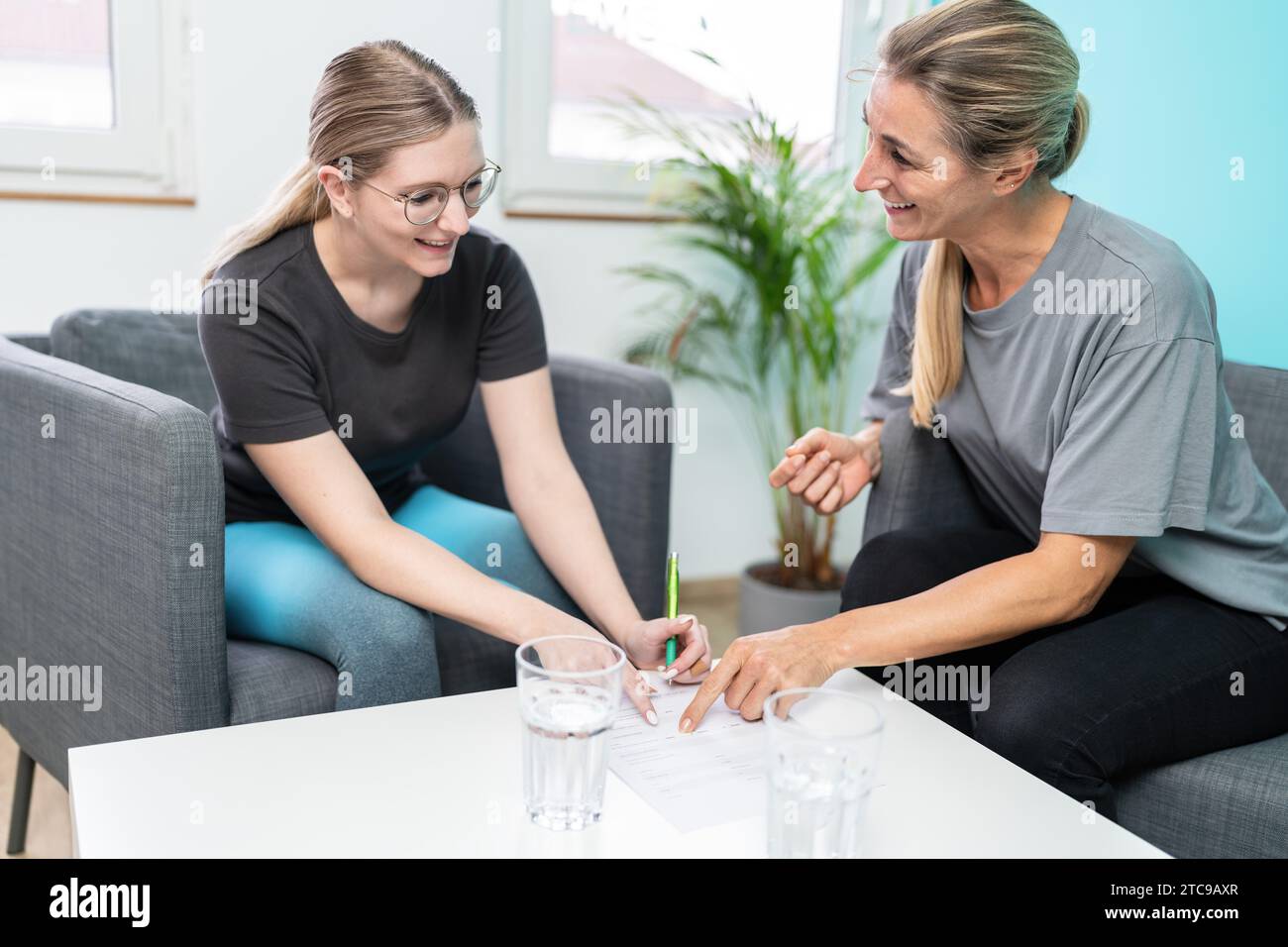 Zwei Frauen lächeln und unterhalten sich mit einer auf einem Formular in einem gut beleuchteten Therapieraum Stockfoto