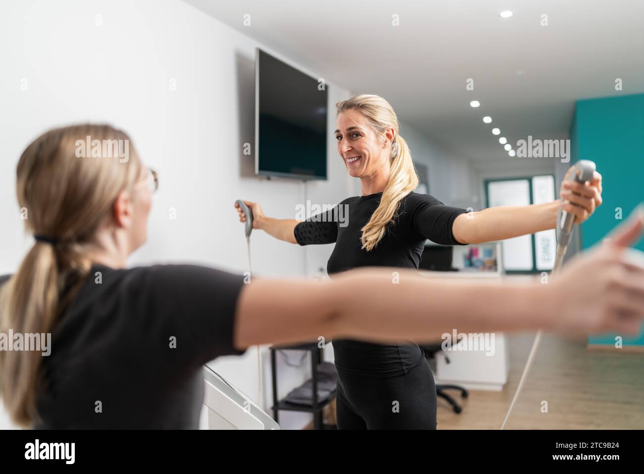 Fitness-Client lächelt, während er den Körper-Kompositionswaage-Analysator hält, führt einen Inbody-Test durch und streckt die Arme in Richtung des Trainers in einem EMS-Studio. Stockfoto