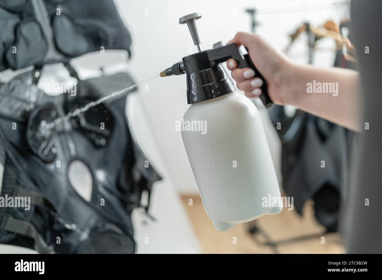 rainer Verwenden Sie eine Sprühflasche, um die ems-Weste mit Wasser für das Training in einem EMS-Studio vorzubereiten Stockfoto