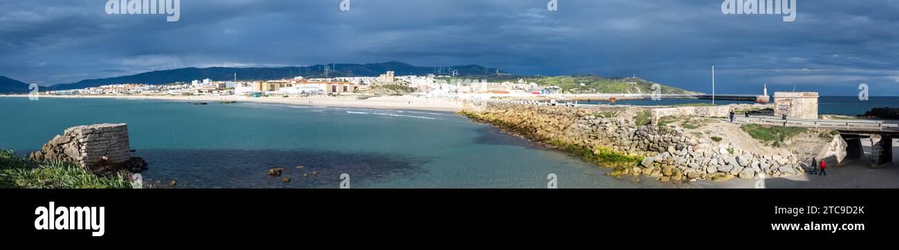 Panoramablick auf eine Küstenstadt mit bewölktem Himmel, ruhigem Meer und einem schützenden Steinbruch. Stockfoto