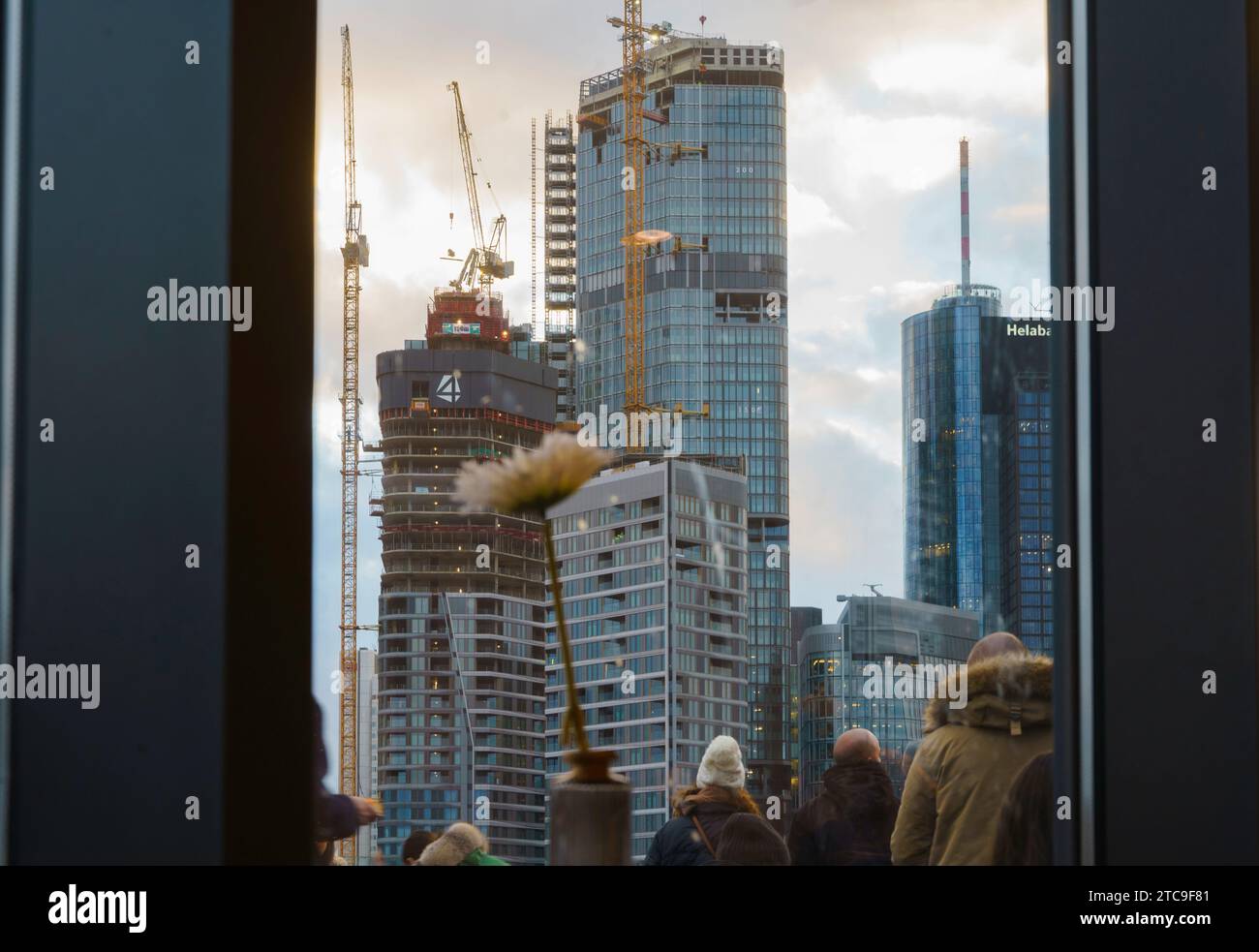 PRODUKTION - 11. Dezember 2023, Hessen, Frankfurt/Main: Die Menschen stehen auf der Terrasse eines Kaufhauses und blicken auf die vier Hochhäuser des Bauprojekts „VIER“. „FOUR“ ist der Name des Bauprojekts auf dem als „Deutsche Bank Dreieck“ bekannten Gelände des Projektentwicklers Groß & Partner Grundstücksentwicklungsgesellschaft. Die Muscheln der vier Hochhäuser sind fast fertig, die Fertigstellung ist für 2025 geplant. Foto: Andreas Arnold/dpa Stockfoto