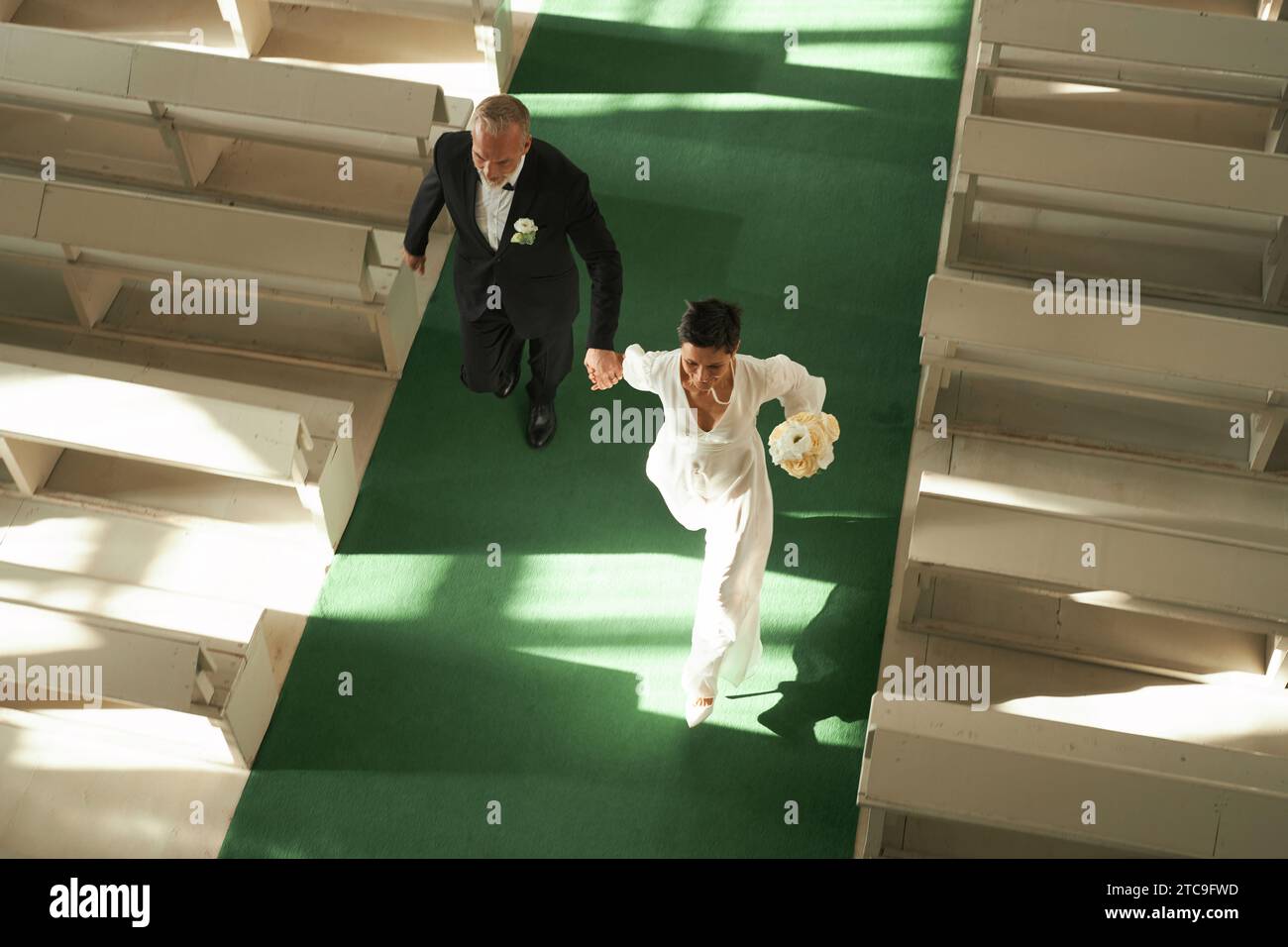 Über dem Blick auf das frisch vermählte Seniorenpaar, das gemeinsam in der Kirche durch Sonnenlicht geht, Kopierraum Stockfoto