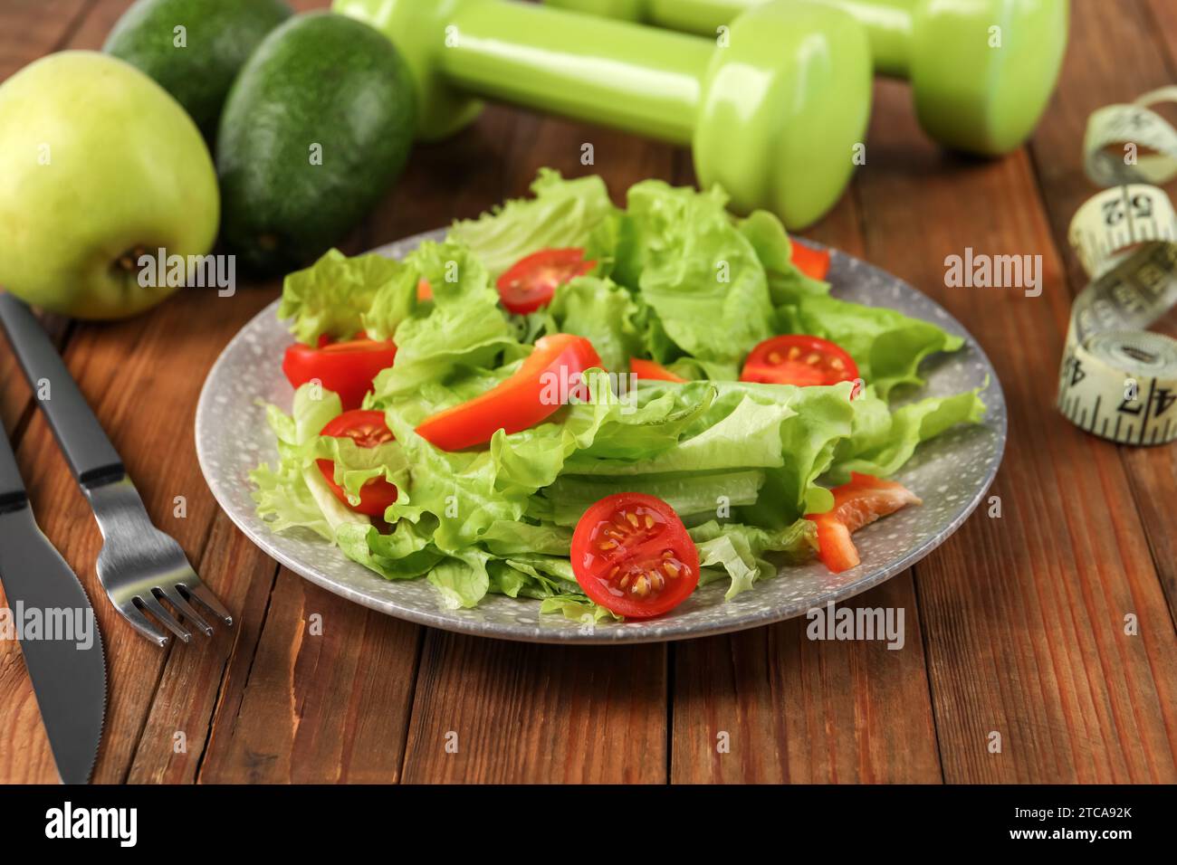 Gesunde Ernährung. Salat, Besteck, Kurzhanteln und Maßband auf Holztisch, Nahaufnahme Stockfoto