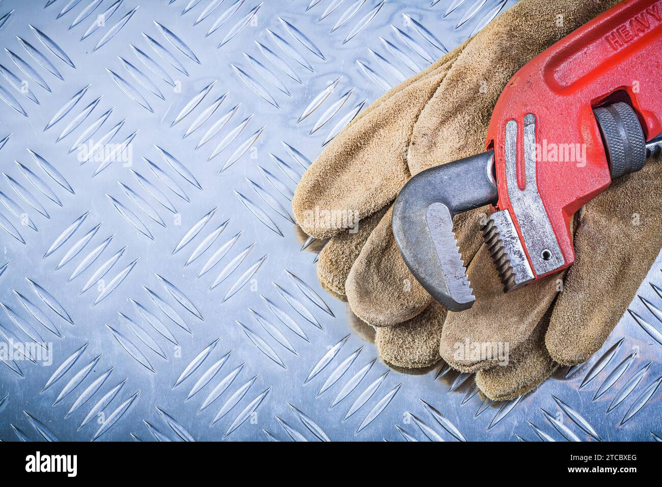 Lederschutzhandschuhe Rohrschlüssel auf kanalförmigem Metallhintergrund Konstruktionskonzept Stockfoto