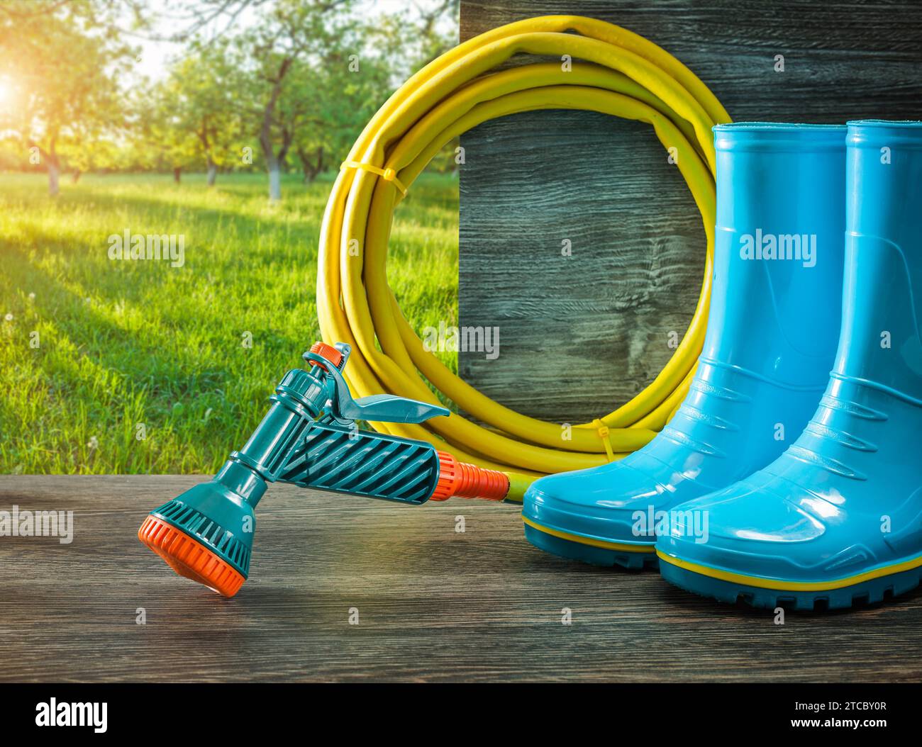 Gartenwerkzeuge Bewässerungsschlauch mit Gan Rain Gummistiefeln auf der Terrasse im sonnigen Frühlingsgarten Stockfoto