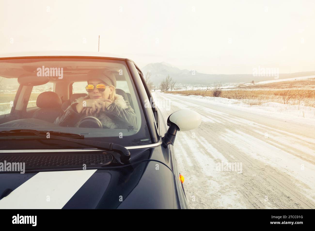 Hipster-Frau in Sonnenbrille, die im Winter in einem kleinen Auto sitzt Stockfoto