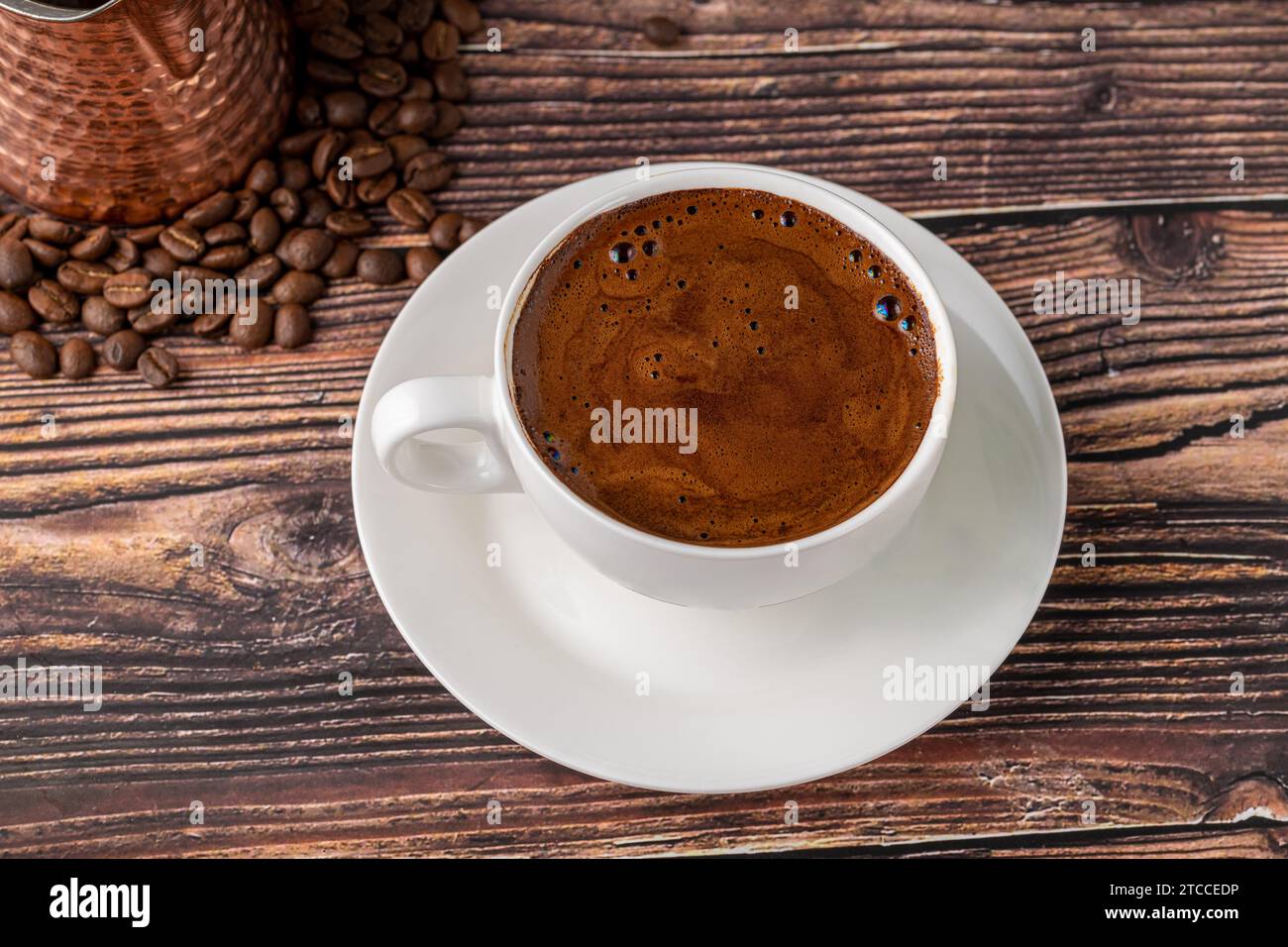 Doppelter türkischer Kaffee in einer weißen Porzellantasse mit dekorativer Kaffeekanne auf einem Holztisch Stockfoto