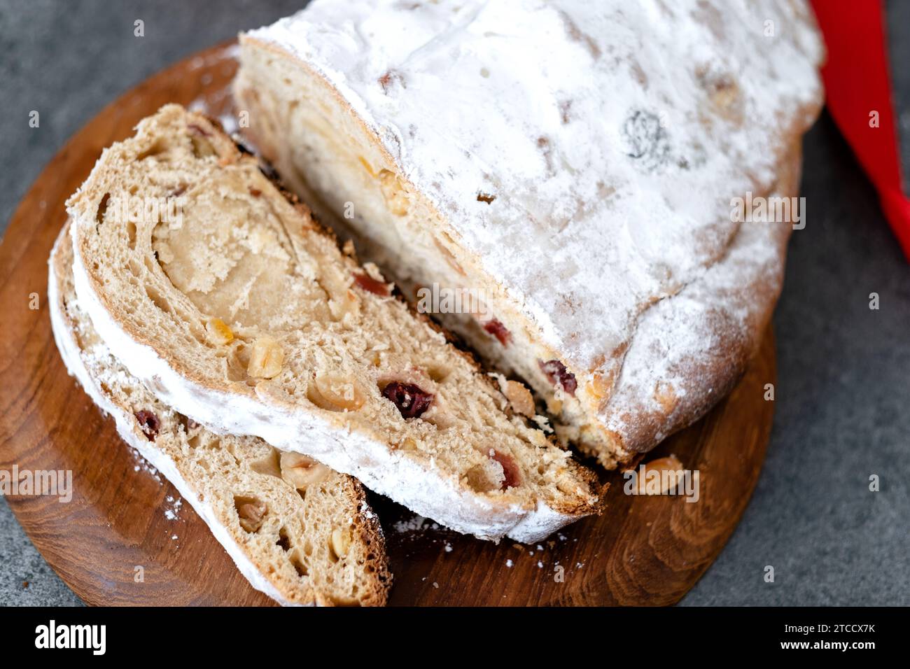 Weihnachtsstollen mit Marzipan, getrockneten Früchten und Nüssen in Scheiben schneiden, mit Puderzucker auf einem Holzbrett bestreut. Feiertagsbacken. Draufsicht Stockfoto