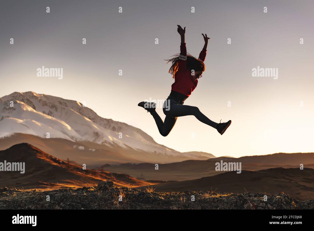 Glückliches, sportliches Mädchen hat Spaß und springt bei Sonnenuntergang gegen schneebedeckte Berge Stockfoto