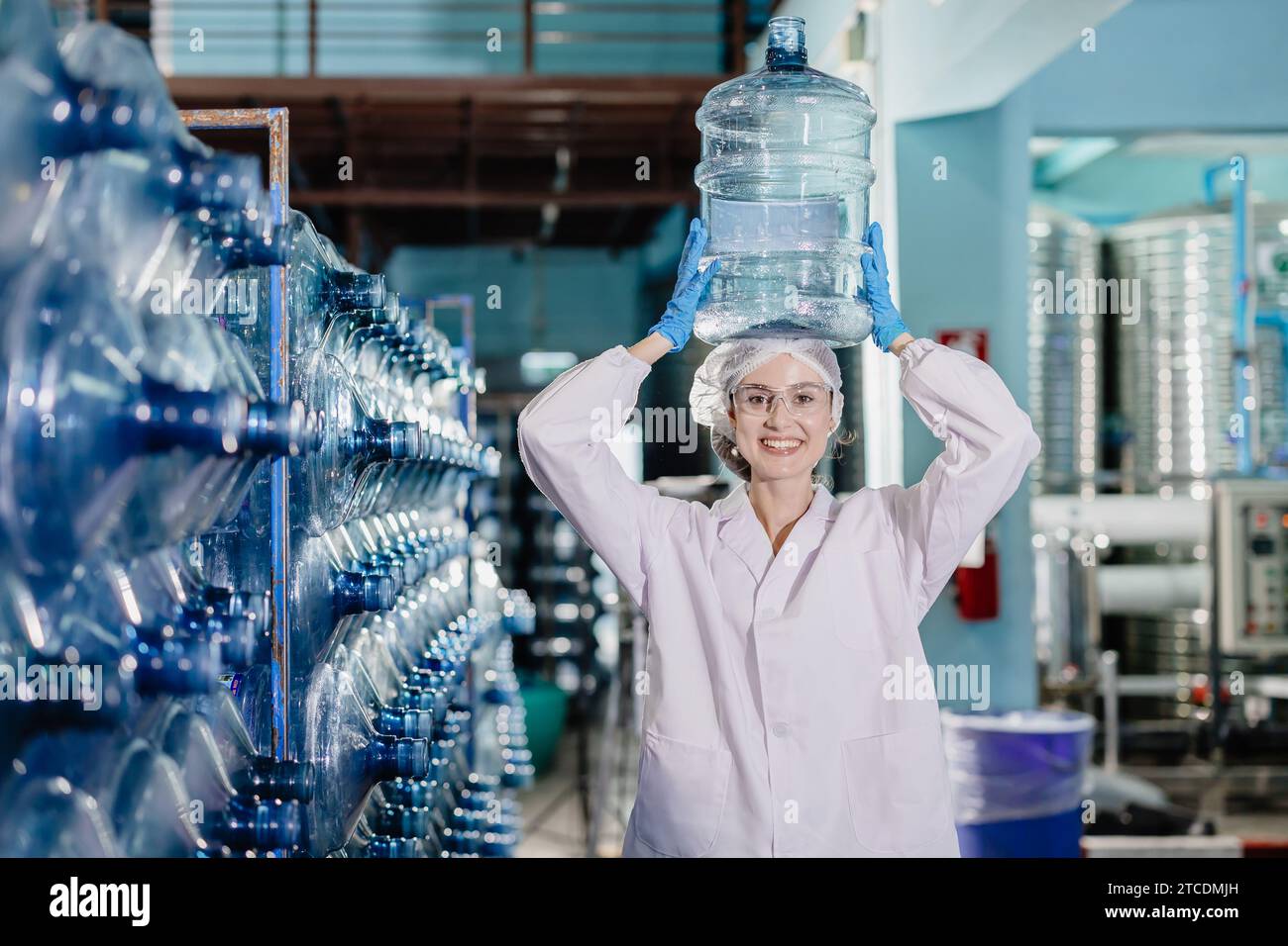 Glückliche Arbeitnehmerinnen arbeiten in der Trinkwasseranlage Fabrik mit Freude Arbeit mit Wasserflasche Gallone im Lager mit Hygieneuniform. Stockfoto