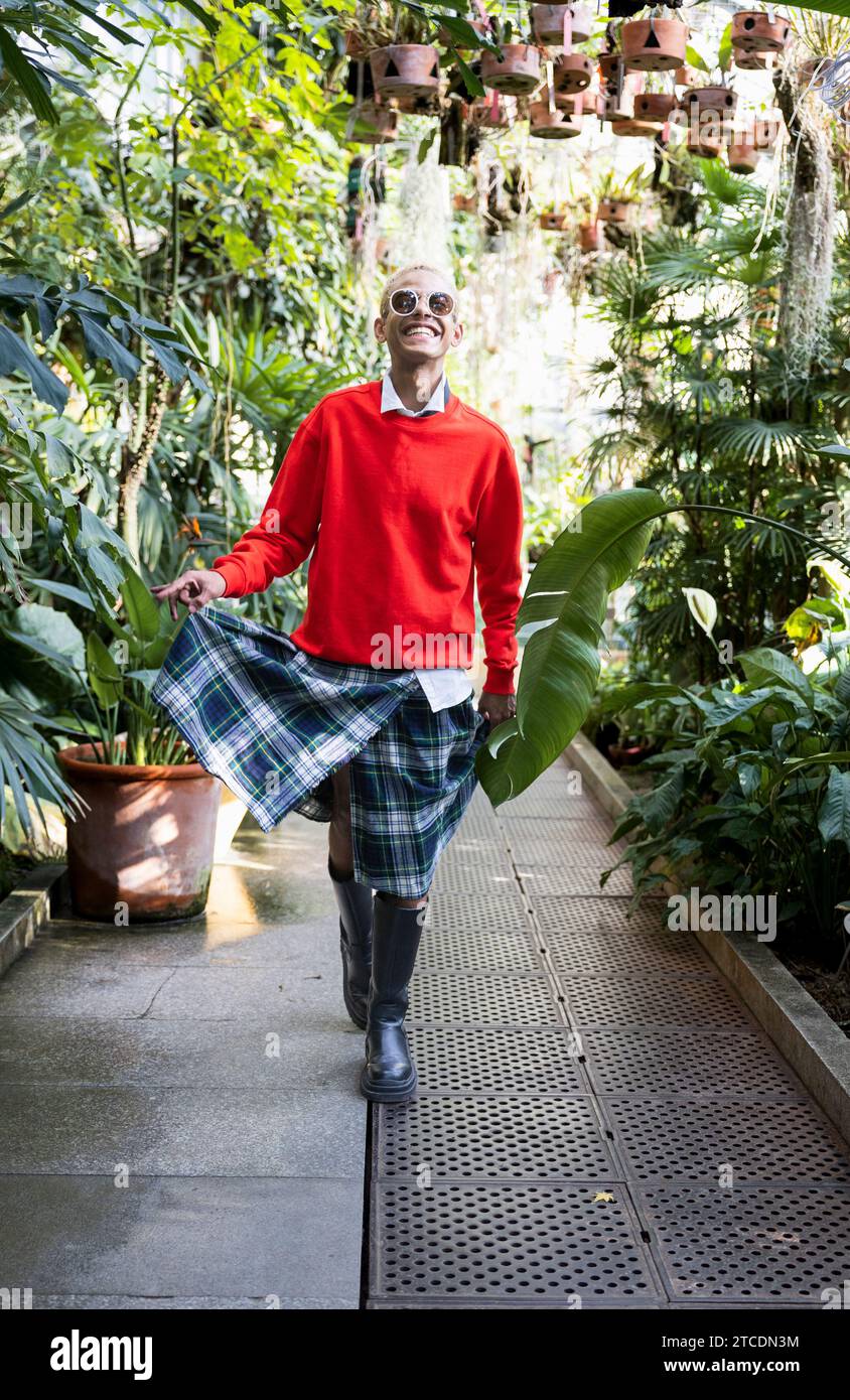 Junger schwarzer Junge lächelnd und fröhlich gekleidet in Kilt im Park Gewächshaus Stockfoto