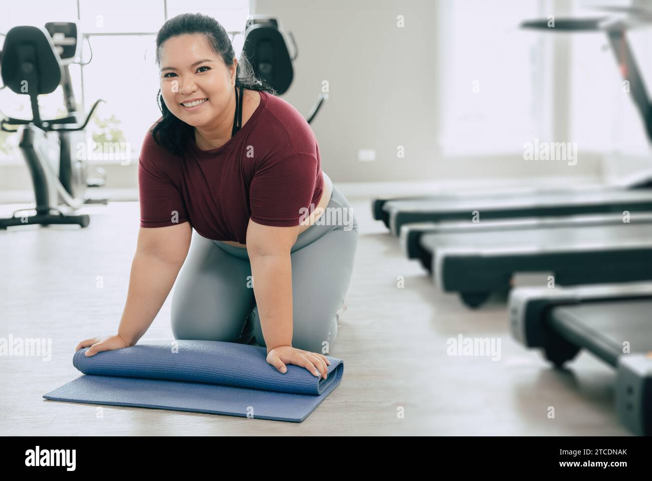 Fette Frau im Fitness-Sportclub Studio mit Yogamatte. Porträt plus Größe weibliche Rolle Pilates Matte glücklich lächelnd nach dem Training. Stockfoto